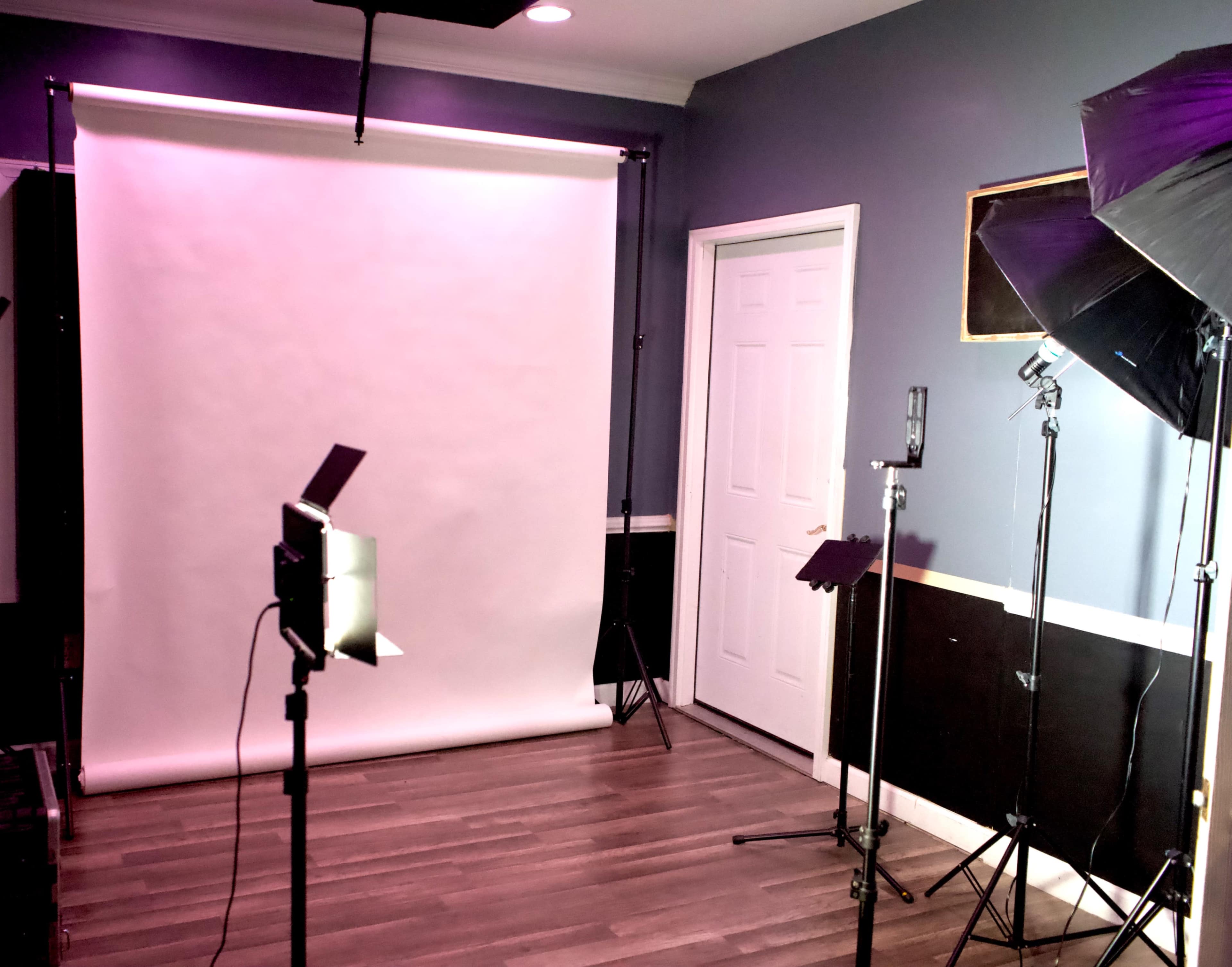 A photography studio setup featuring a seamless backdrop, lighting equipment, and music stands arranged in the room.