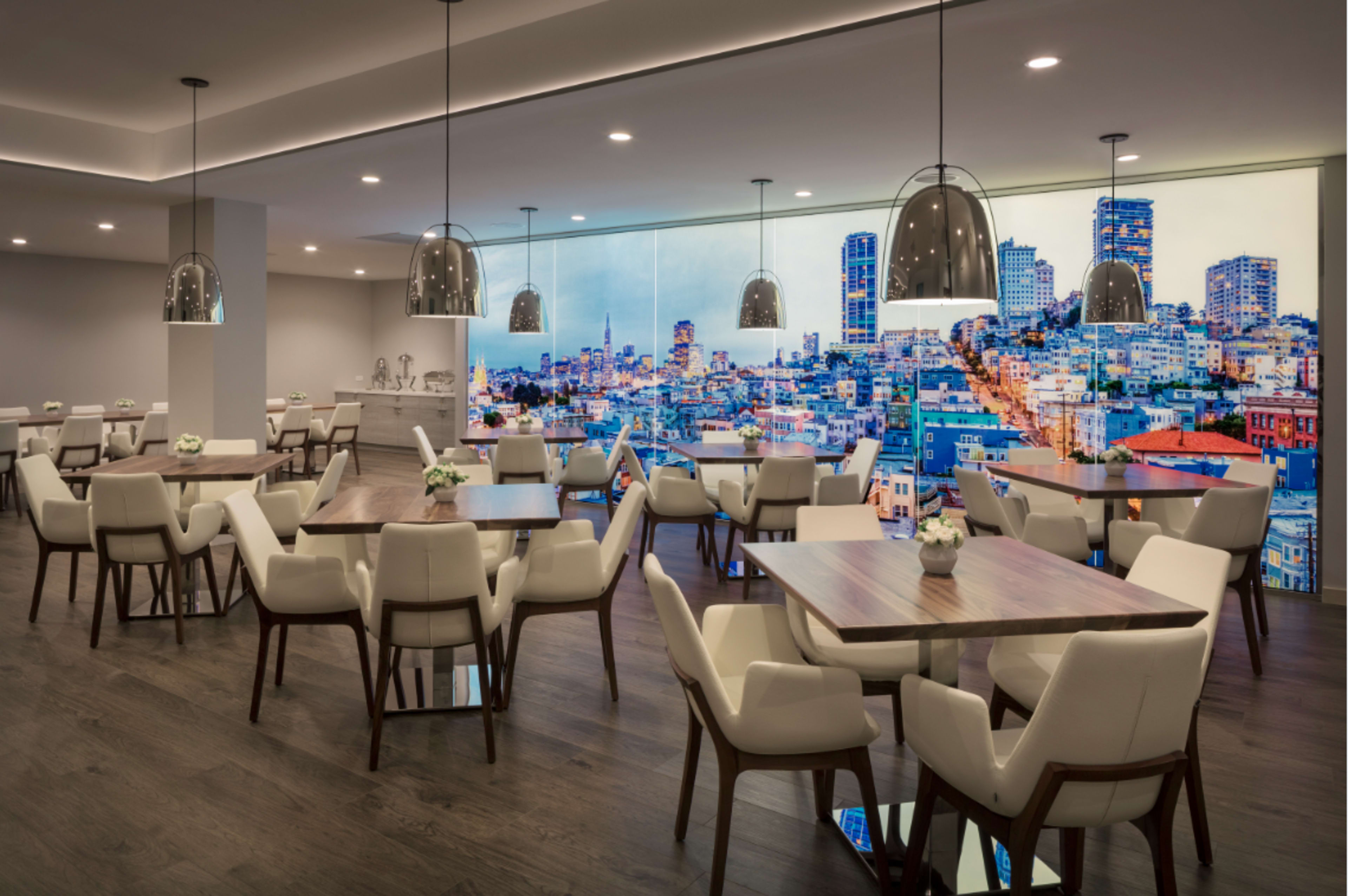 A modern dining area with several tables and chairs, featuring a large wall mural of a city skyline.