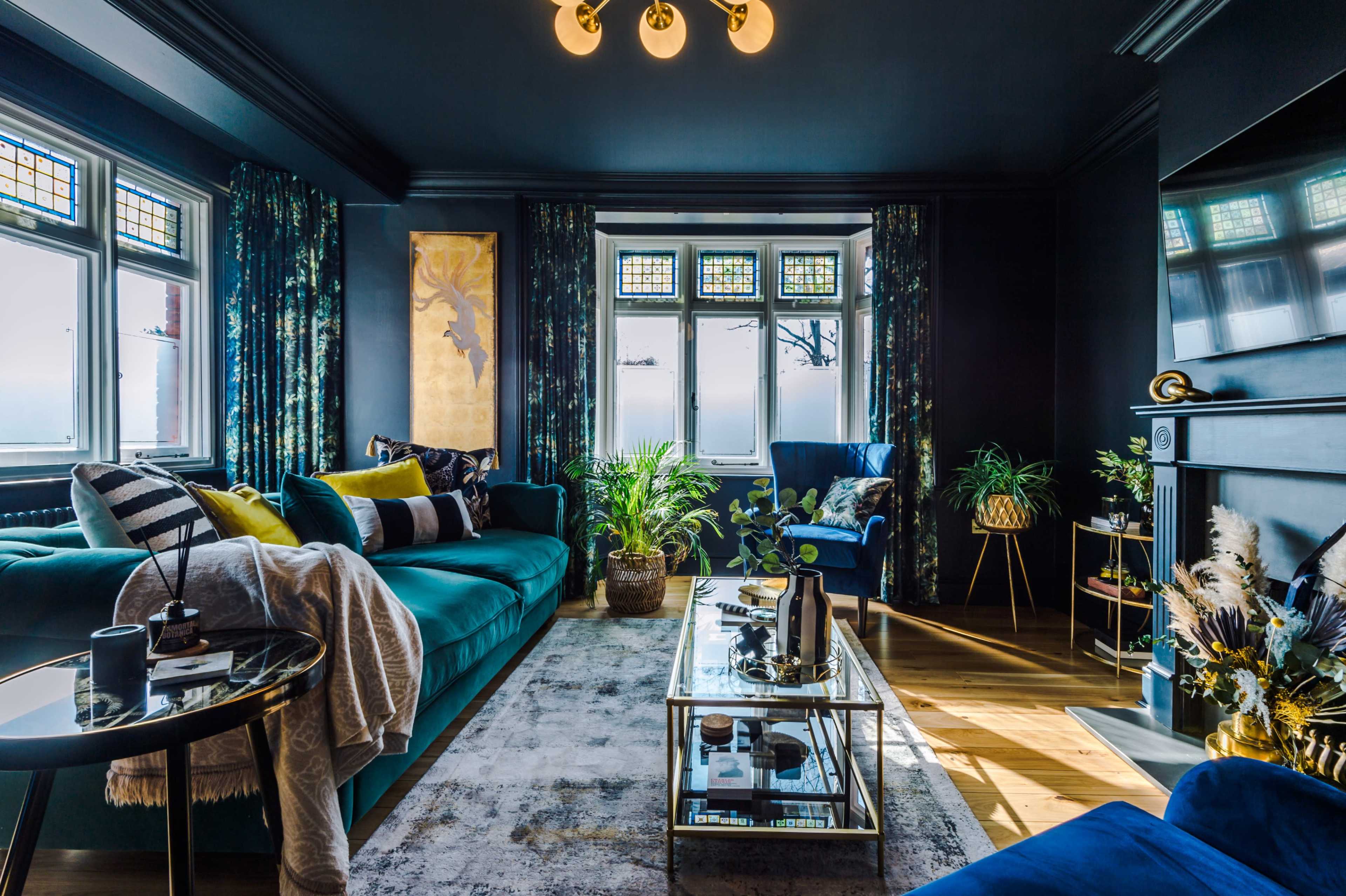 A modern living room featuring a deep blue sofa, a glass coffee table, and large windows adorned with patterned curtains.