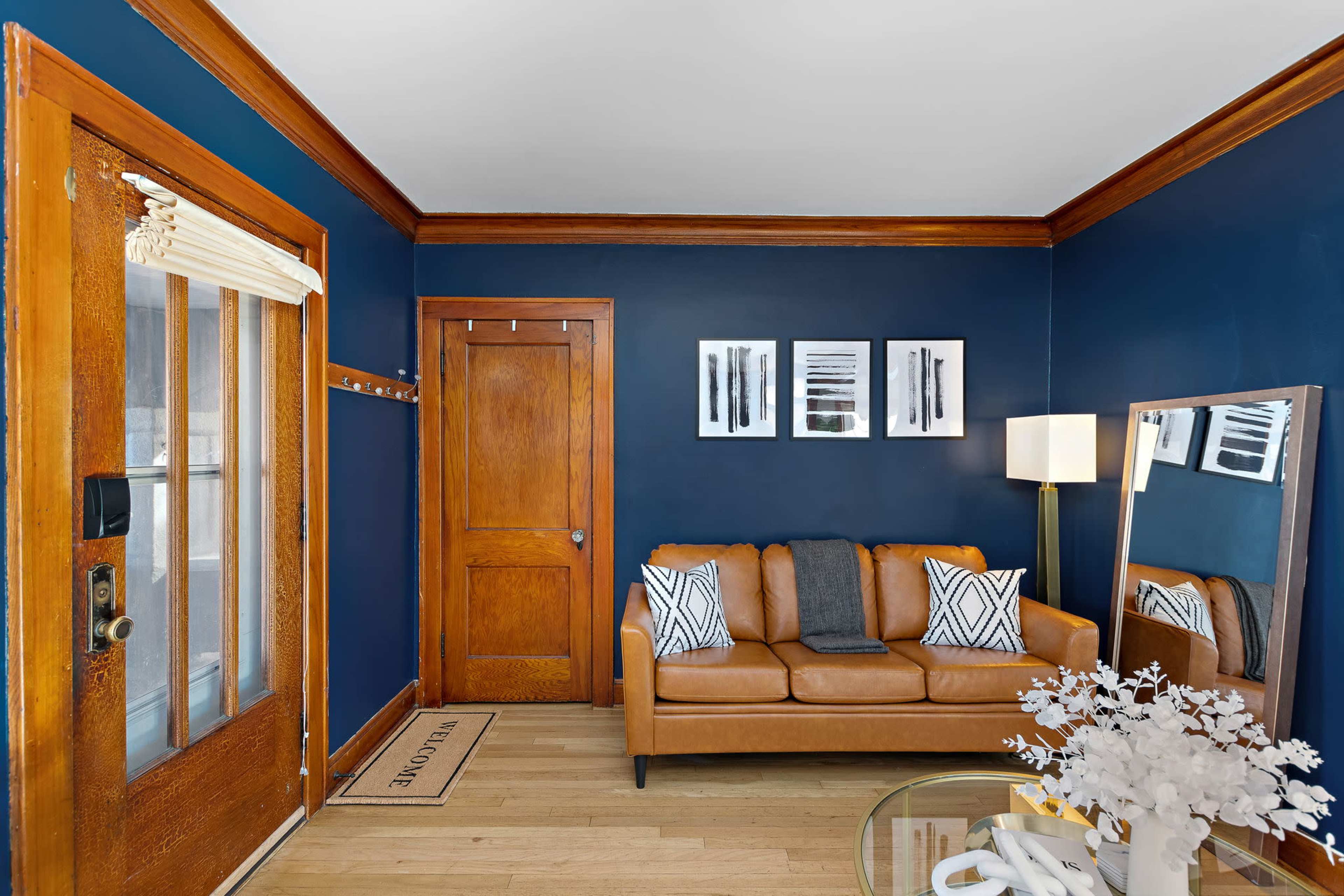 A cozy living room features a brown leather sofa, a round glass coffee table, and dark blue walls with wooden trim.