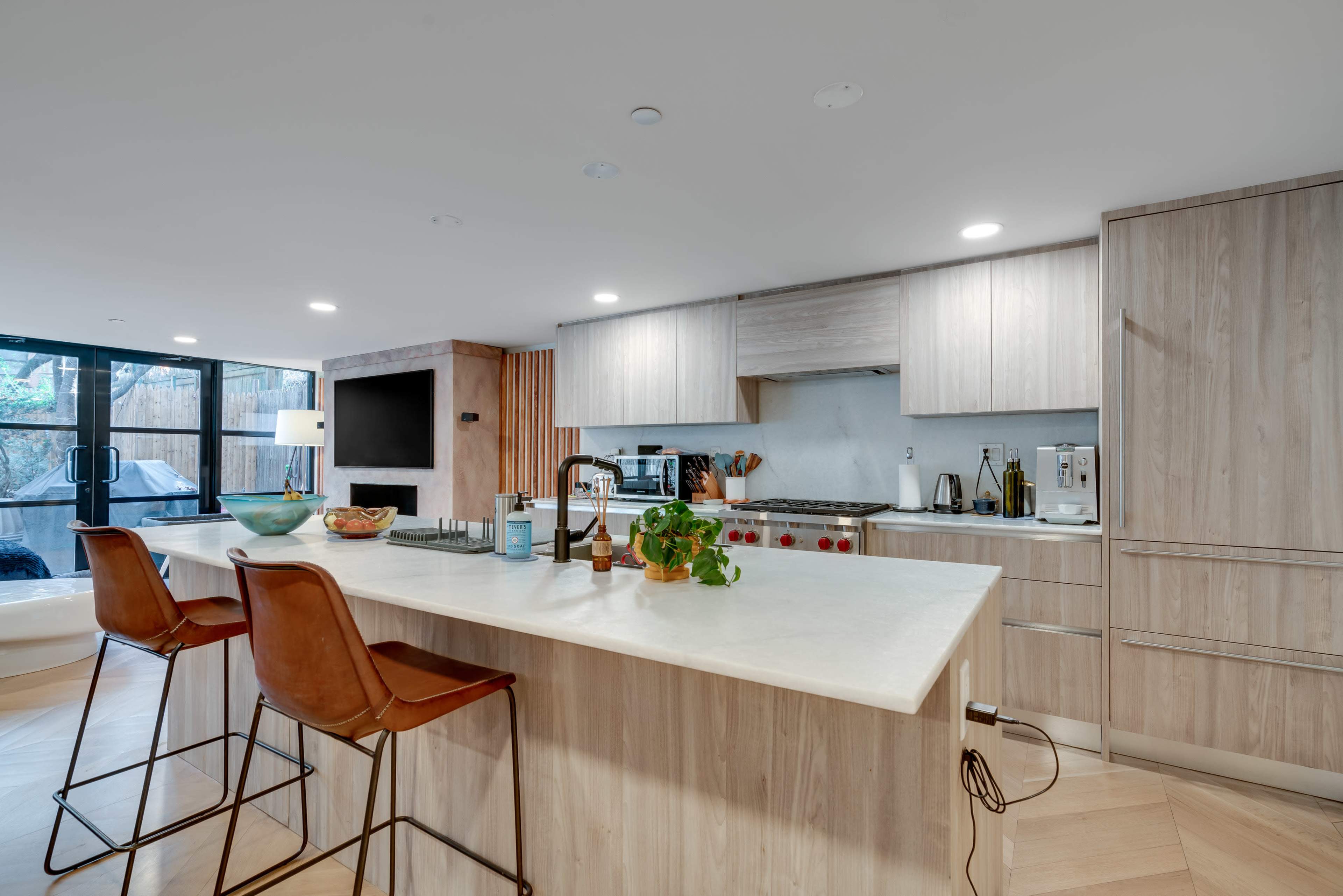 A modern kitchen features a large island with bar stools, sleek cabinetry, and stainless steel appliances.