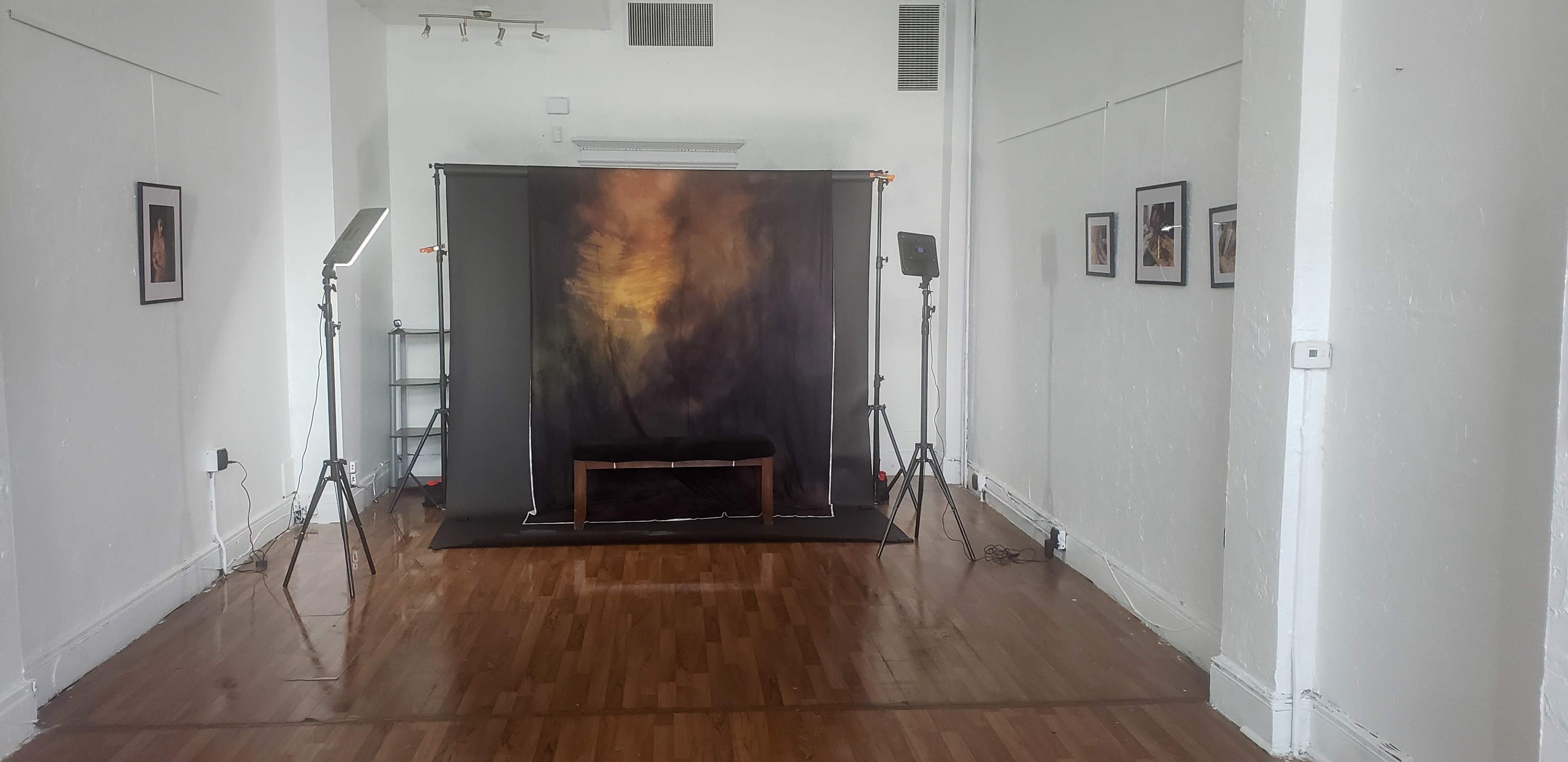 A photography studio with a backdrop, a bench, and lighting equipment set up in a spacious, empty room.