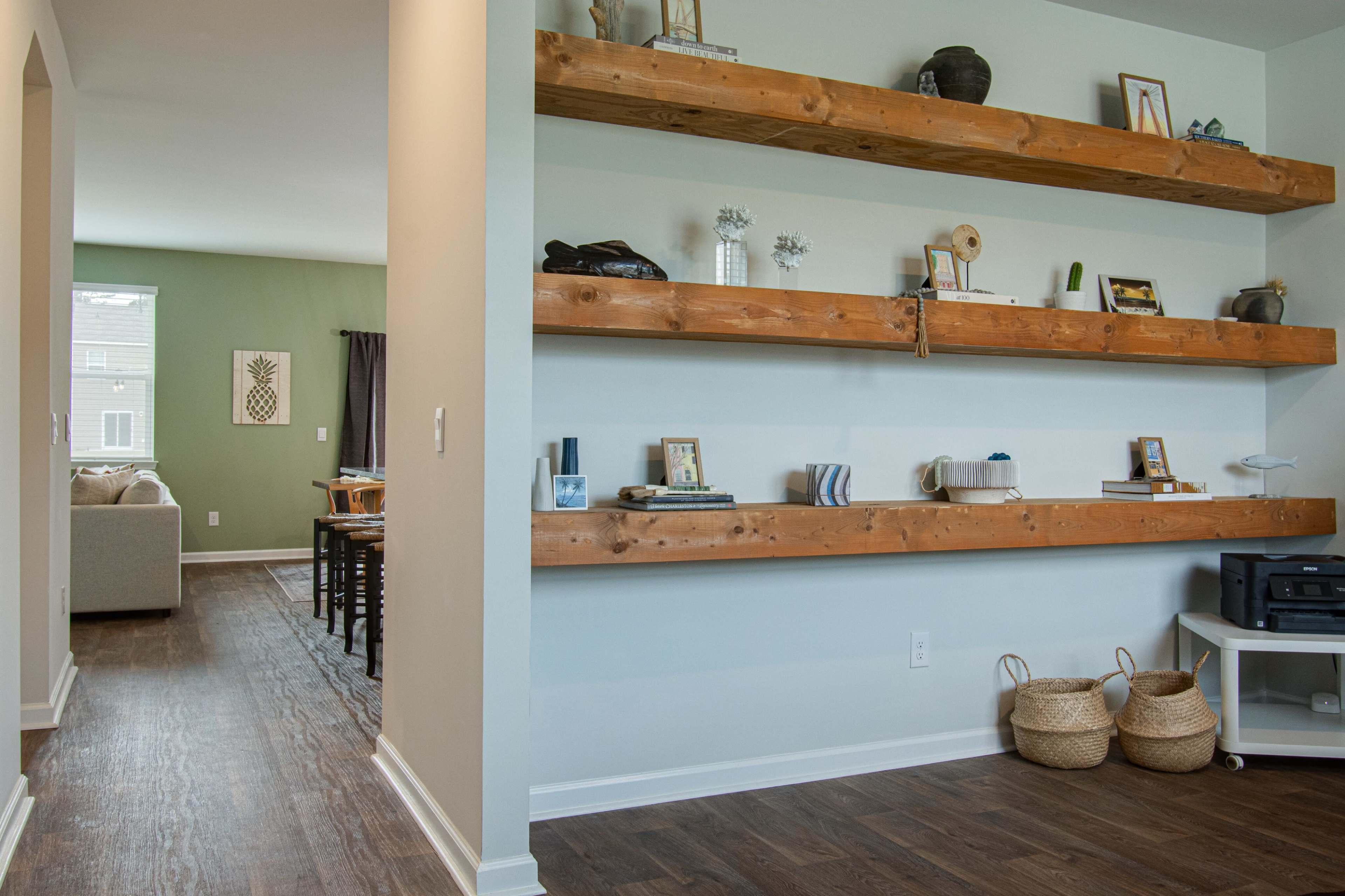 An interior space featuring a wall with wooden shelves holding various decorative items, alongside a view of an adjacent room with a couch and dining area.