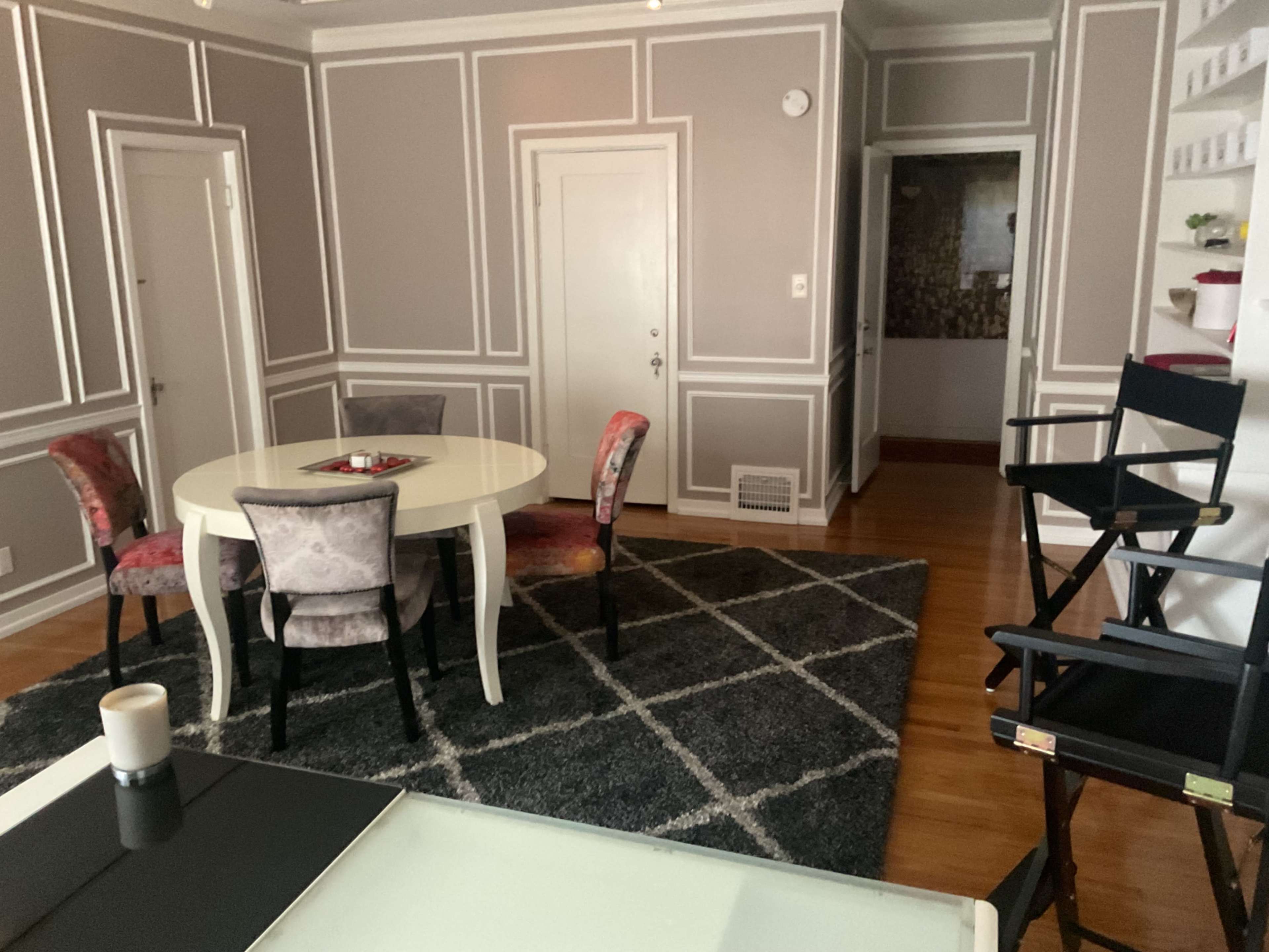 The image shows a room with a round dining table surrounded by four chairs, a gray area rug, and two doorways leading to other spaces.