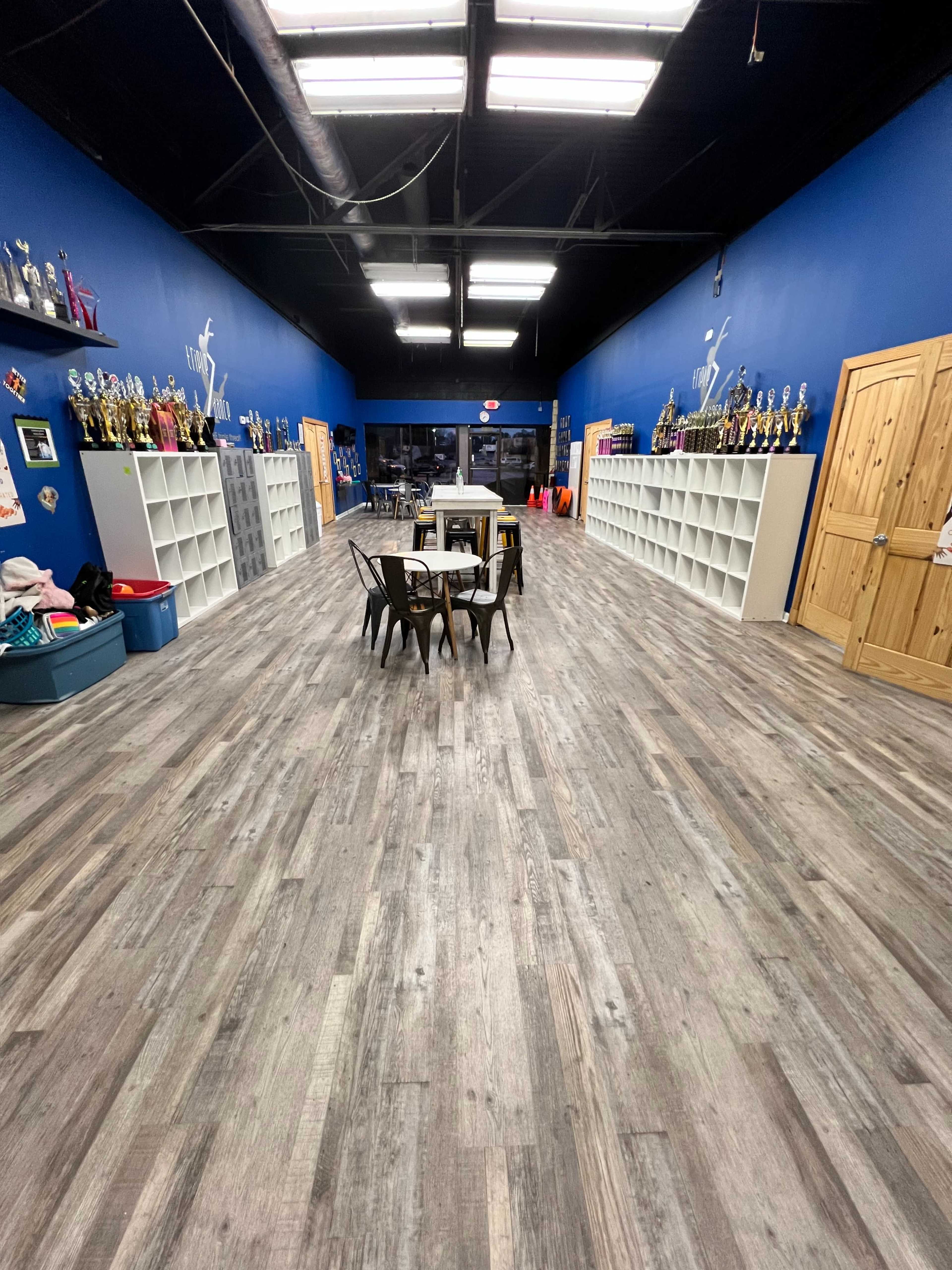 A long, narrow room with blue walls, shelves filled with trophies along the sides, and a table with chairs in the center.
