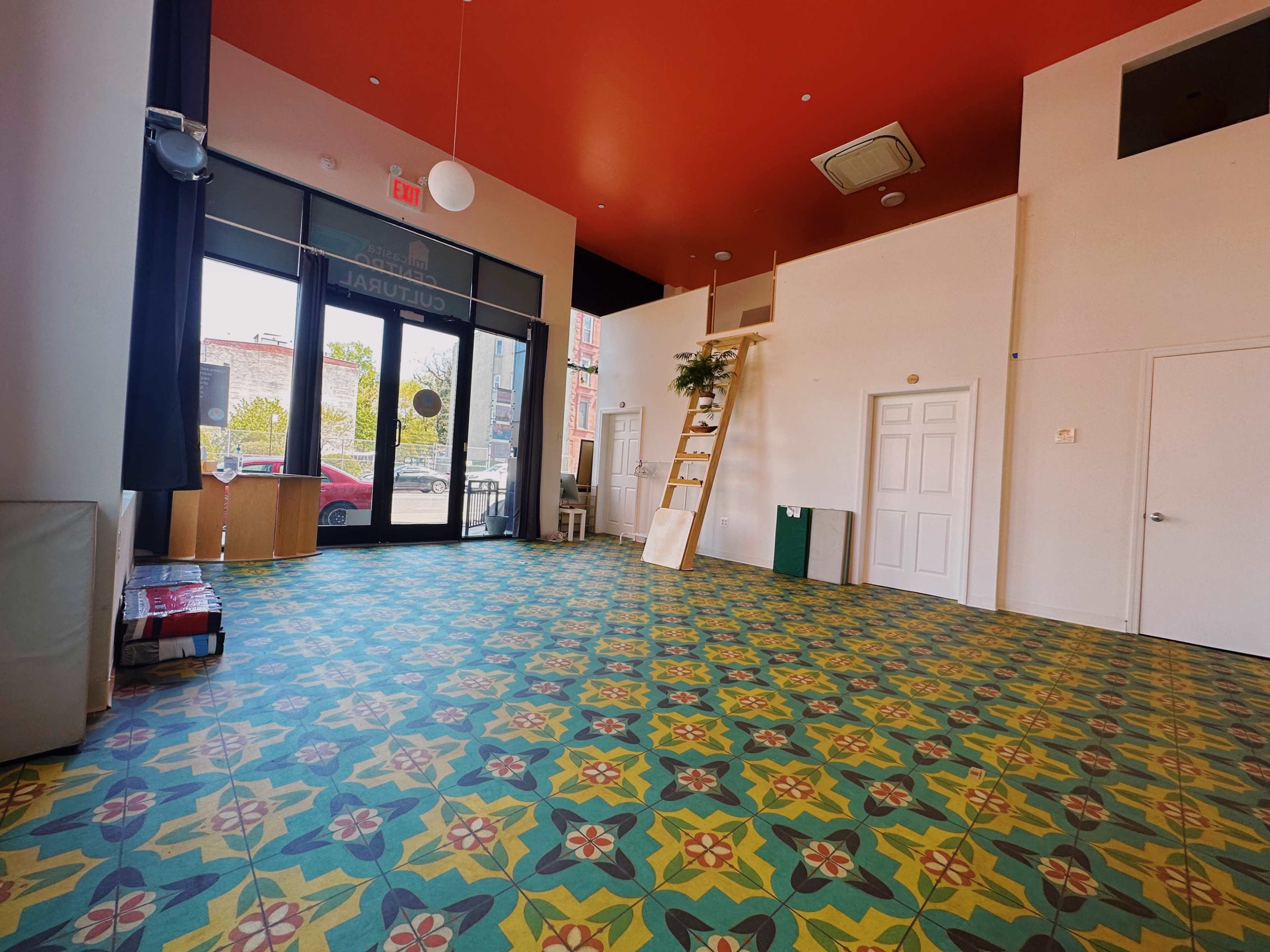 A spacious room with patterned tile flooring, large windows letting in natural light, and a lofted area accessed by a ladder.