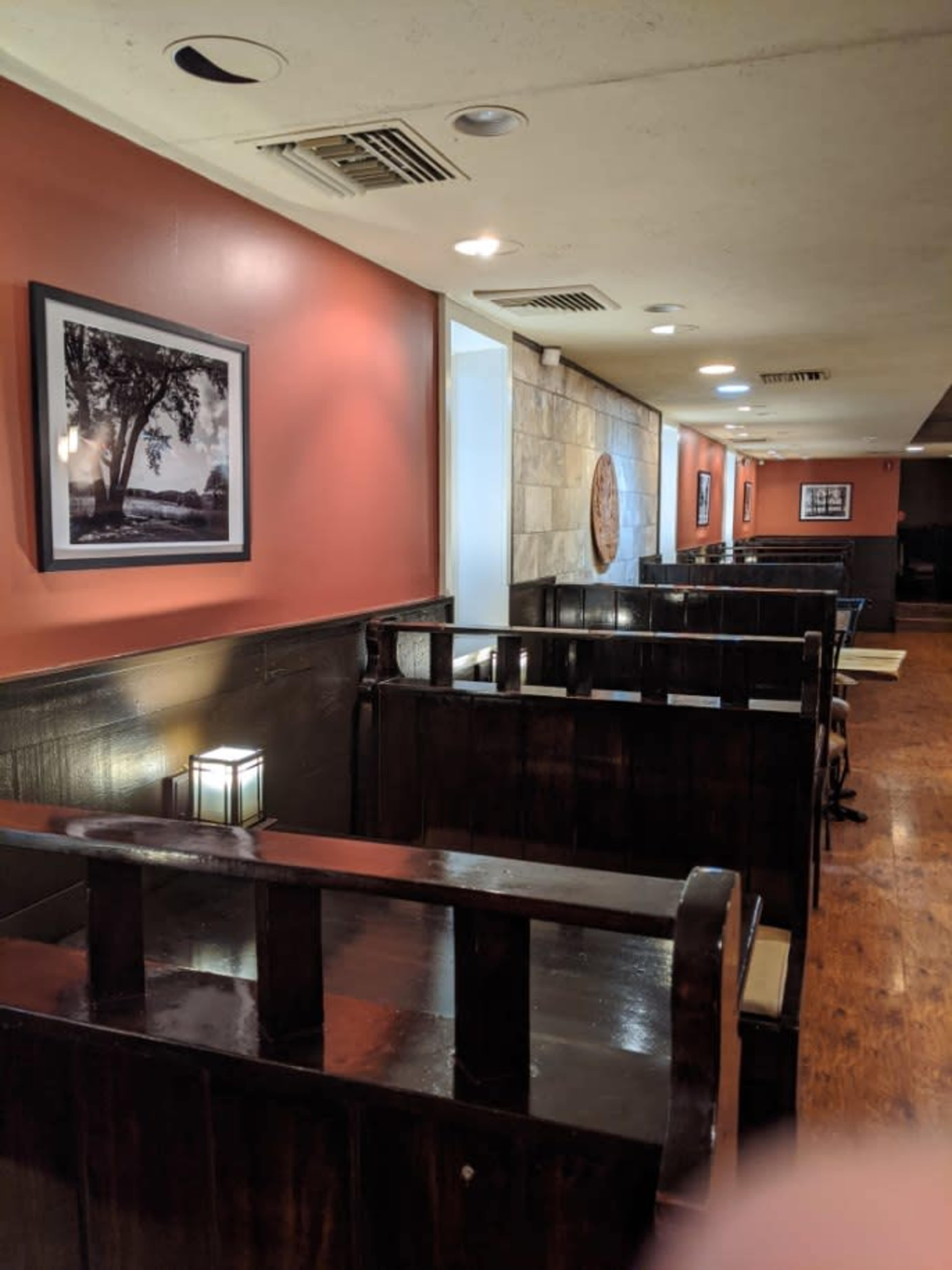 A long hallway in a restaurant with wooden booths, framed black-and-white photographs on the walls, and a warm lighting fixture on each booth.