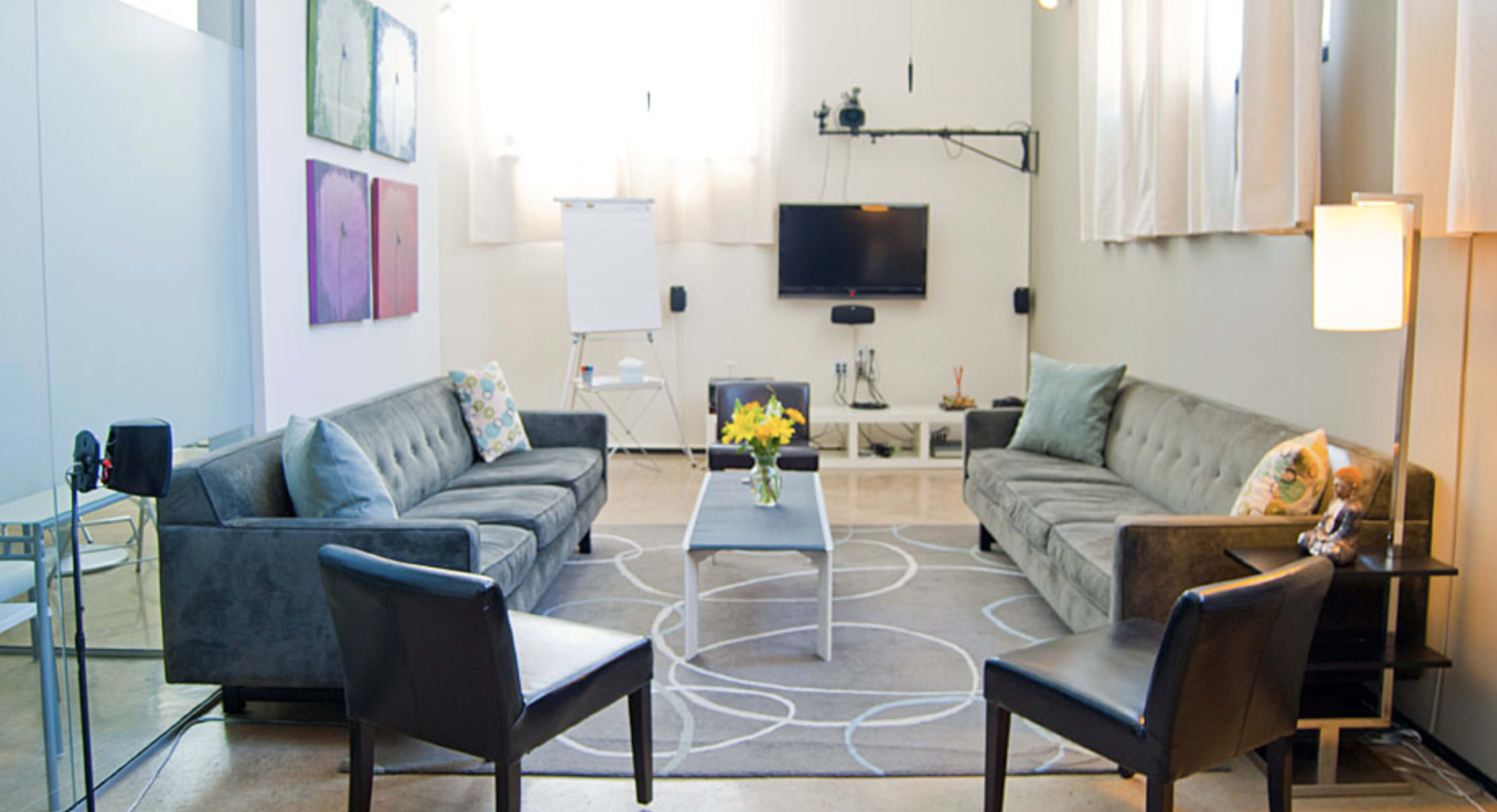 A modern living room with two sofas, a coffee table, a television, and a floral arrangement on a light-colored rug.