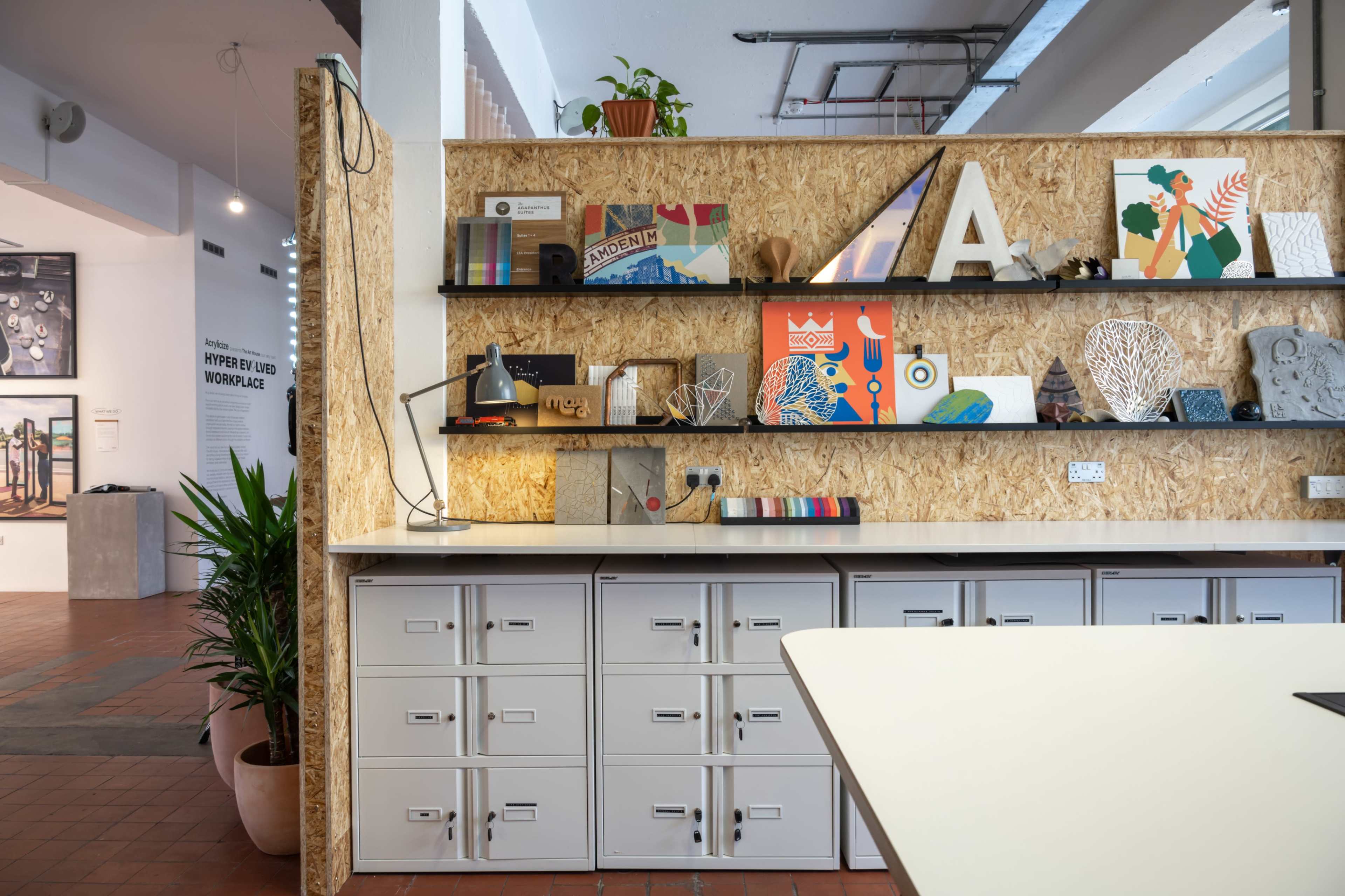 A modern workspace featuring a wooden wall with decorative shelves displaying various art pieces and design objects, alongside metal filing cabinets.