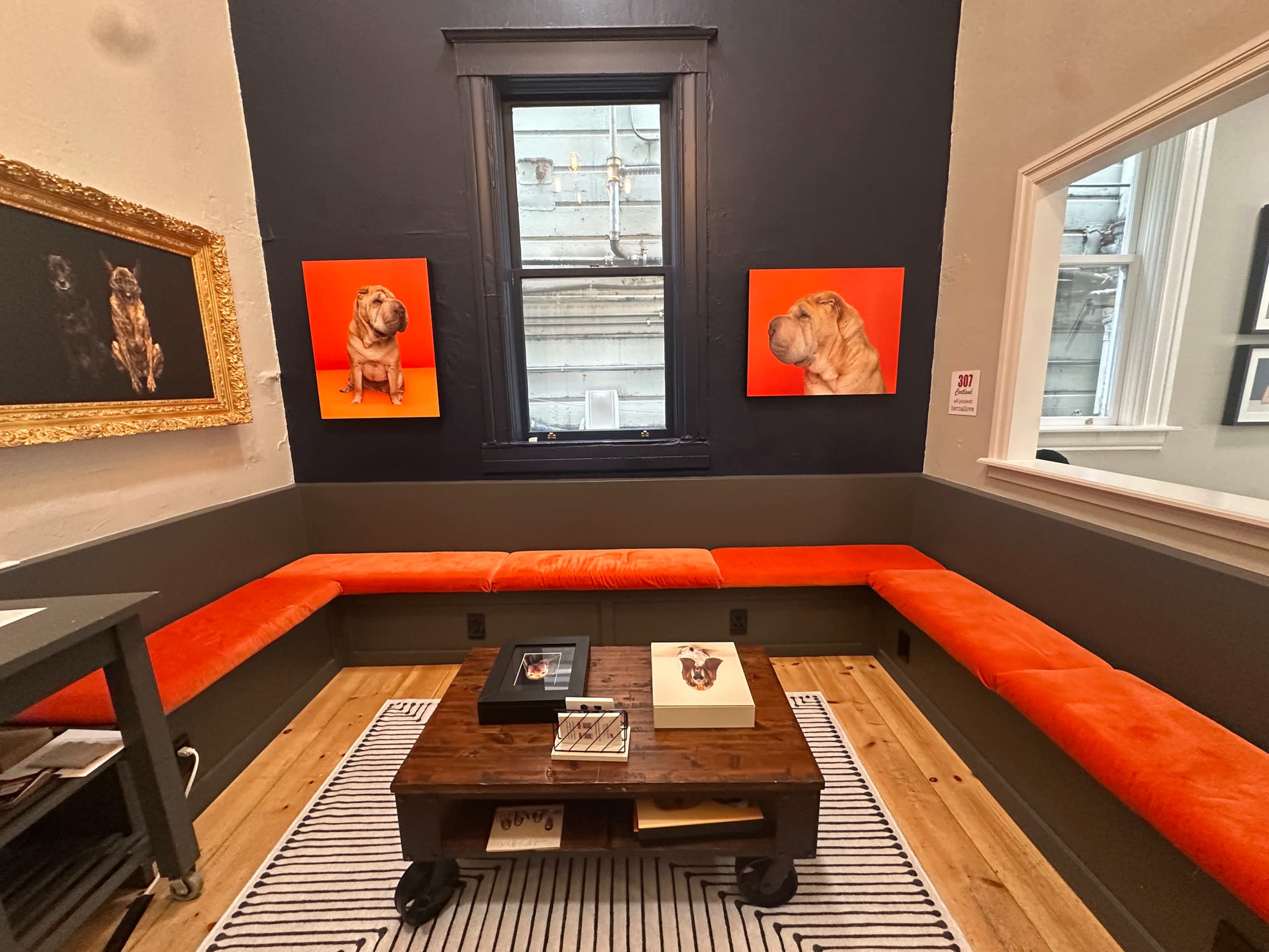 The image shows a cozy room with orange leather seating, two large dog portraits on orange backgrounds, and a wooden coffee table on a striped rug.