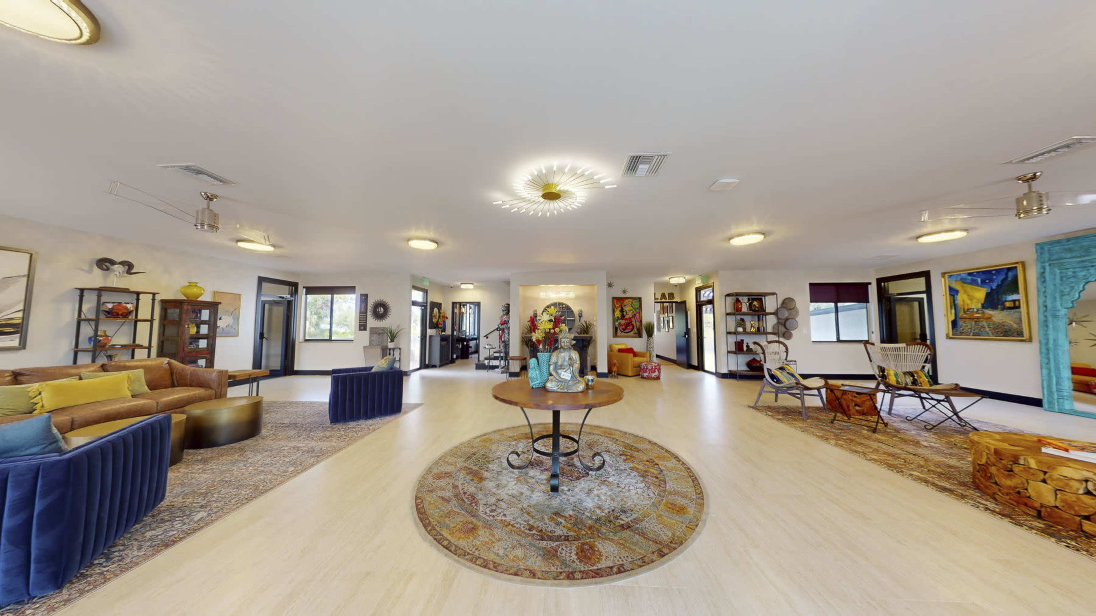 A spacious, well-lit indoor area with a mix of seating arrangements, decorative art pieces, and a central circular rug.