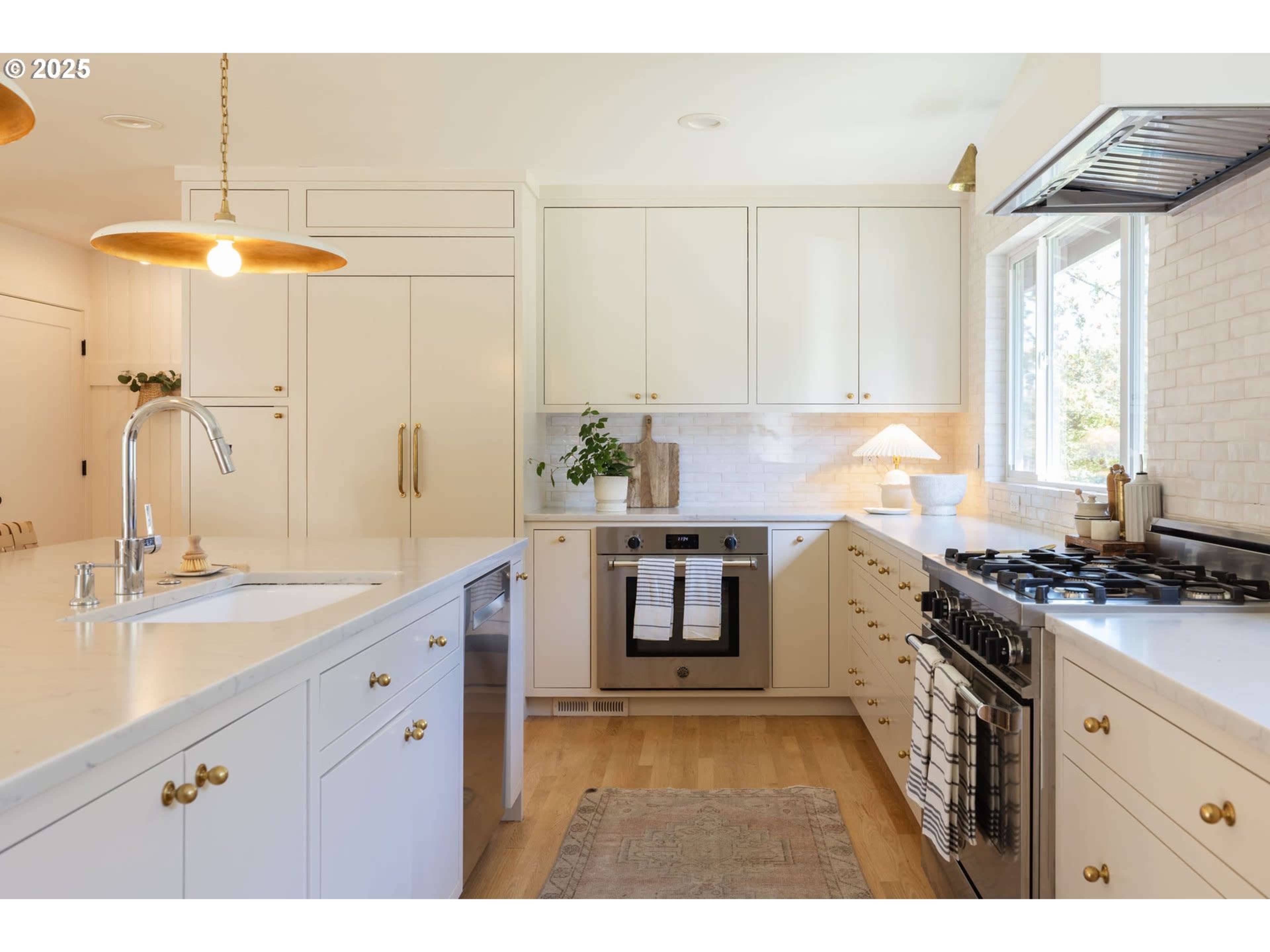 The image shows a modern kitchen with white cabinets, a marble countertop, and stainless steel appliances.