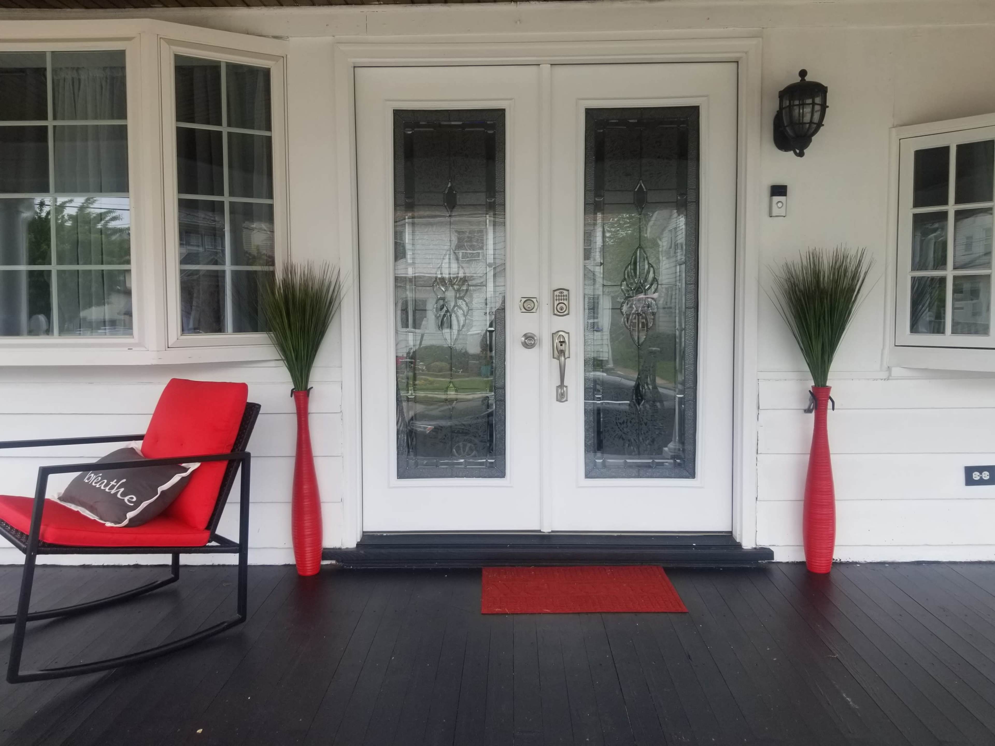 A front porch with a pair of decorative red vases, a red chair, and double glass doors with ornate patterns.