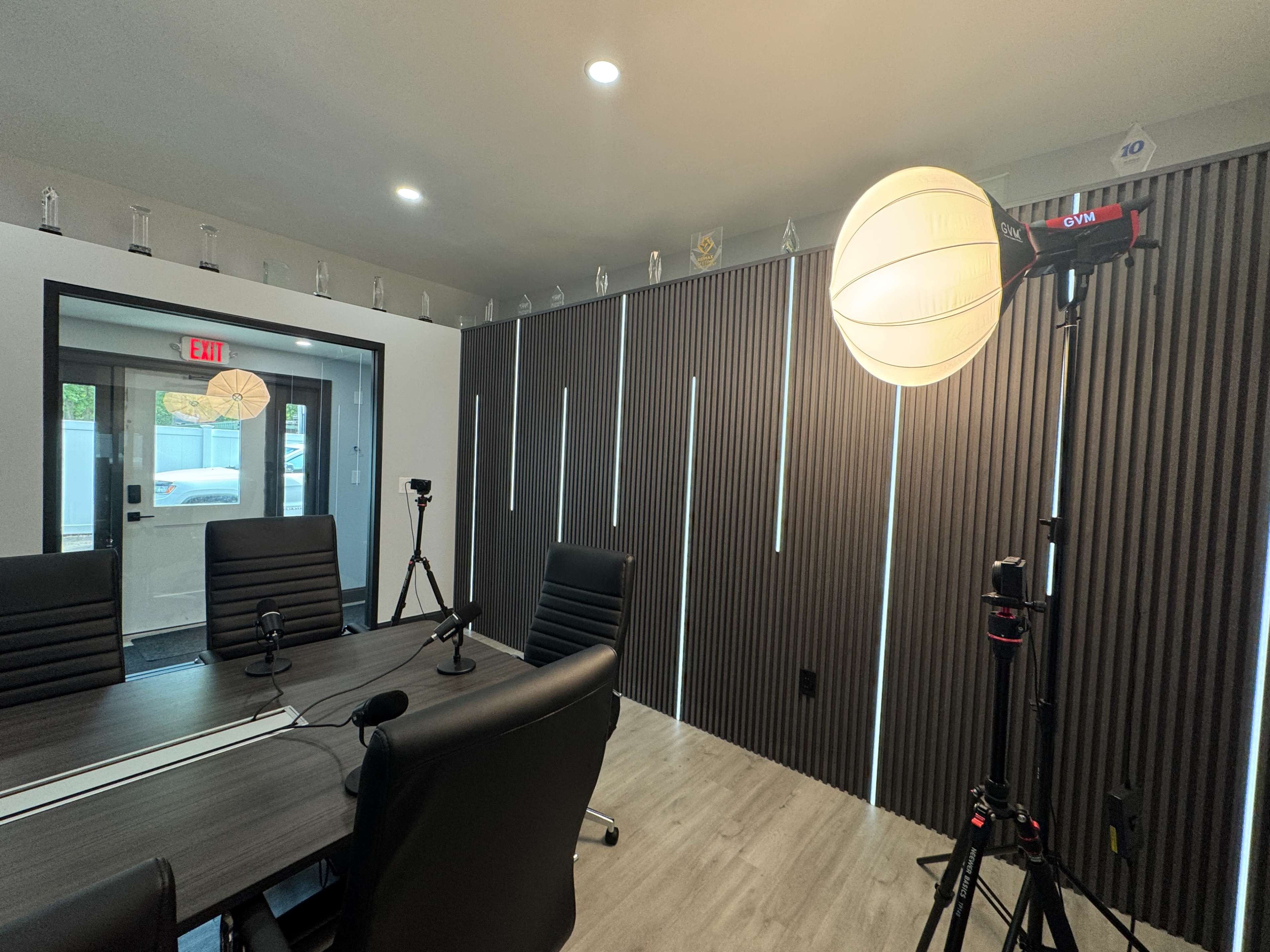 The image shows a modern conference room with a large table, black chairs, and a softbox light set up beside the door, illuminated with vertical lights on the wall.