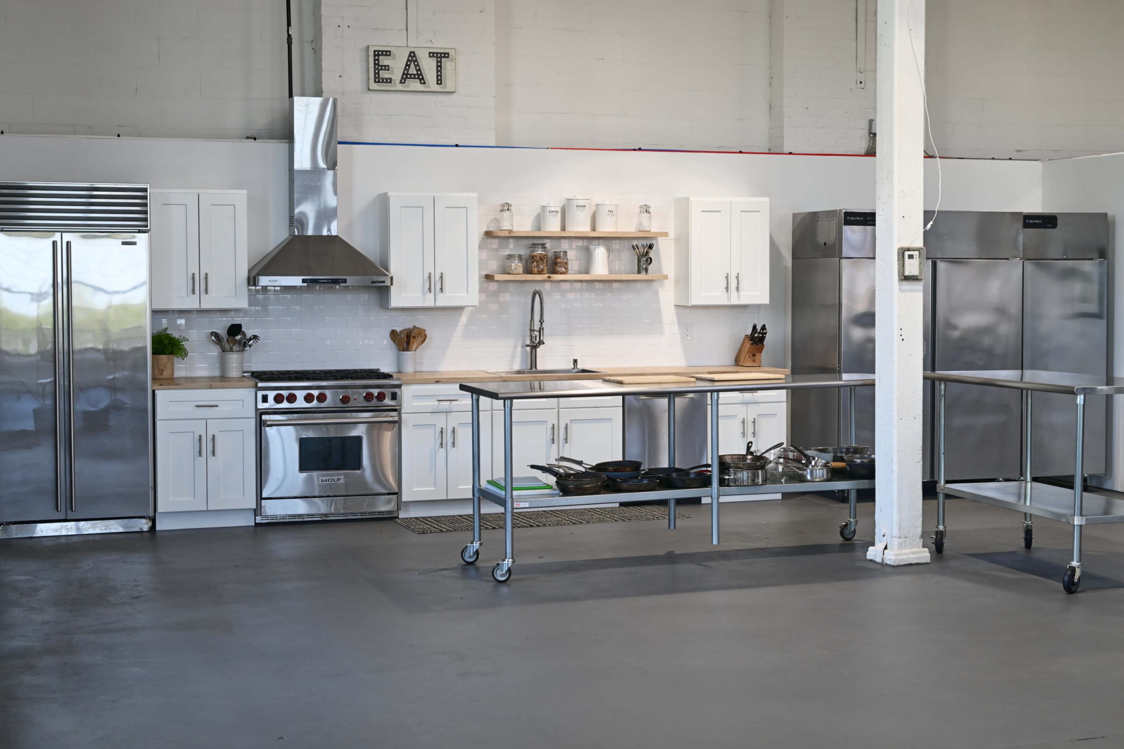 The image shows a modern kitchen with stainless steel appliances, white cabinetry, and a central island on wheels.