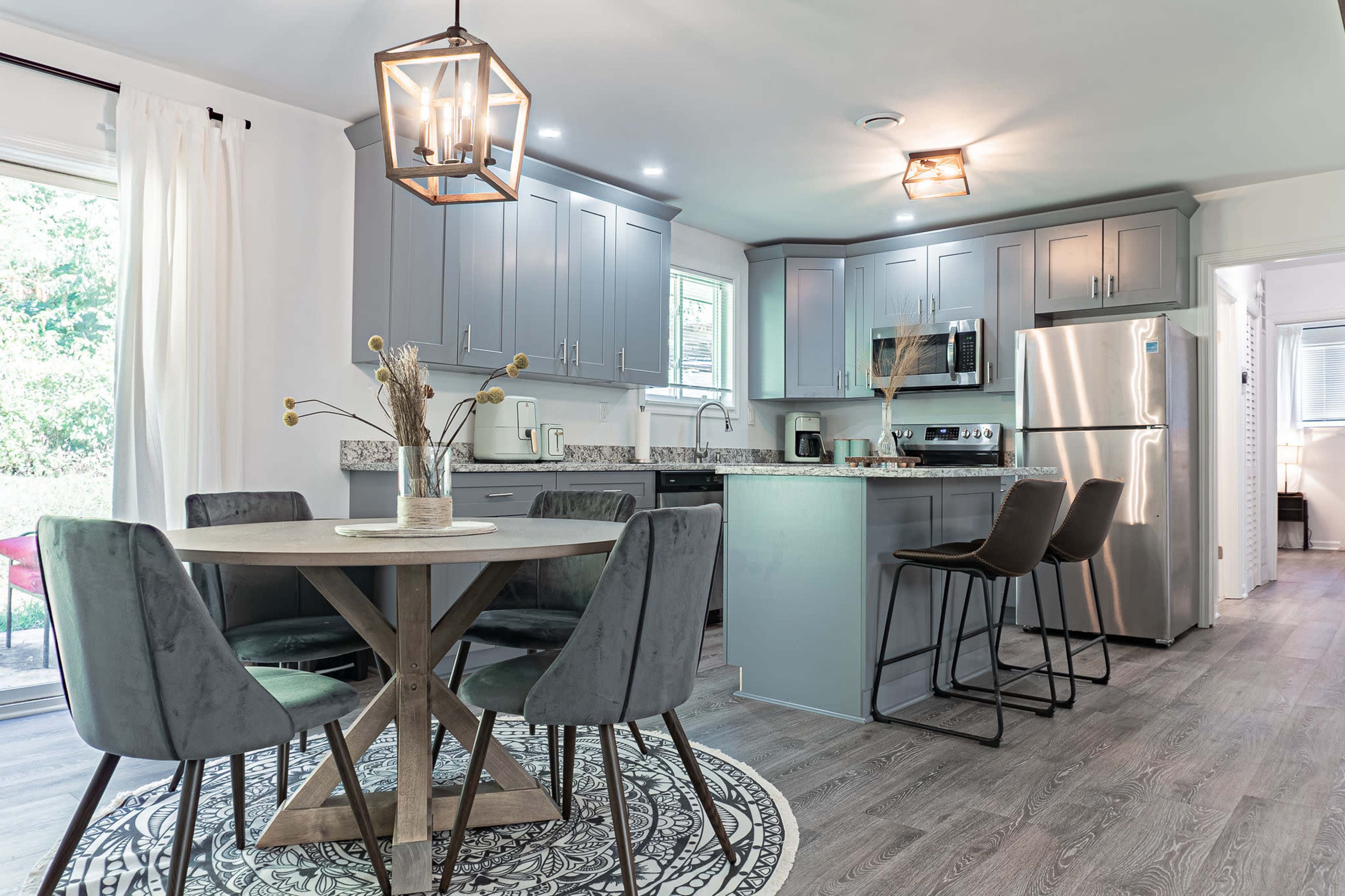 A modern kitchen with gray cabinetry, a round wooden table set with black chairs, and stainless steel appliances, complemented by a decorative rug on the floor.