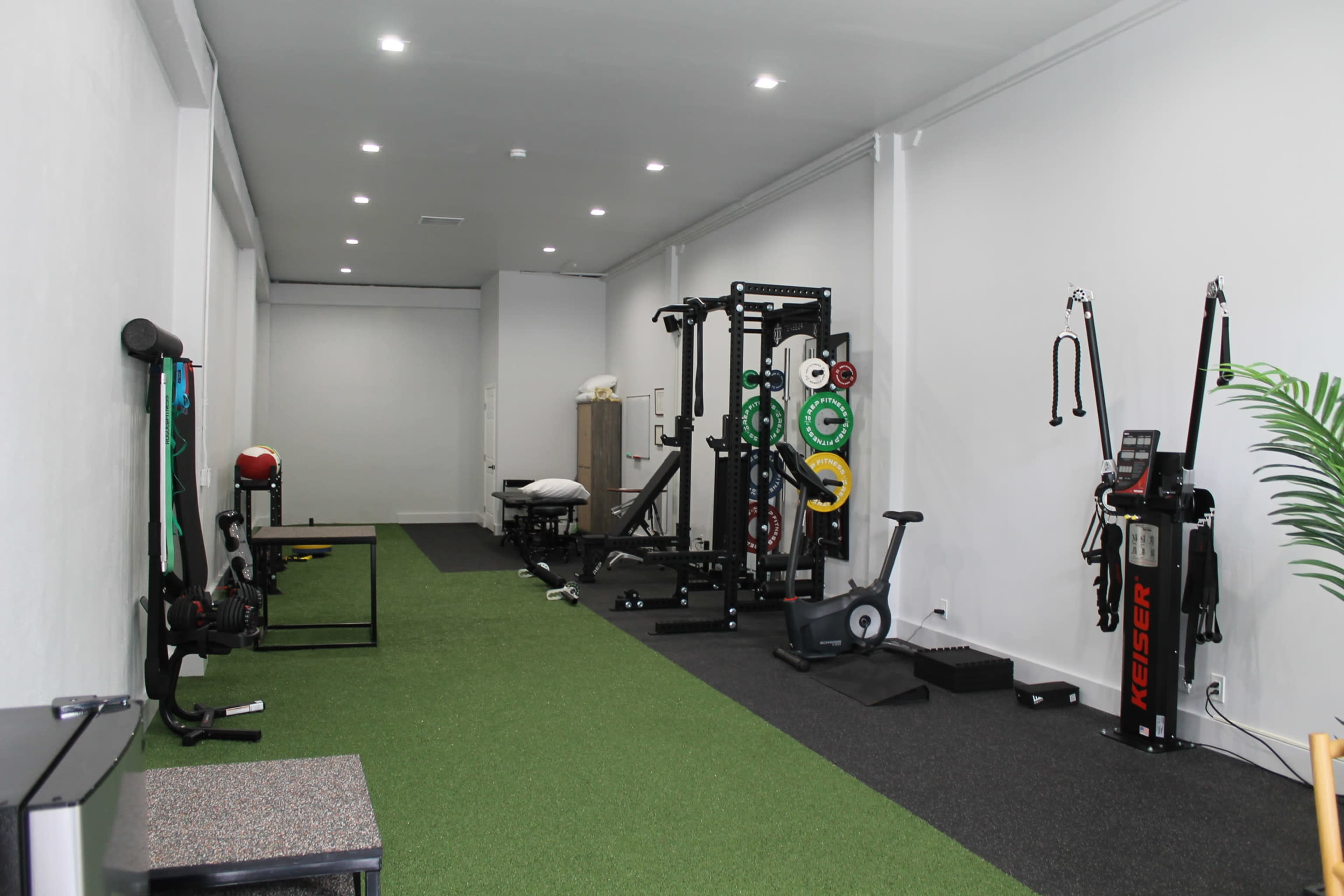 A modern gym interior with turf flooring, various workout equipment, and a spacious layout.
