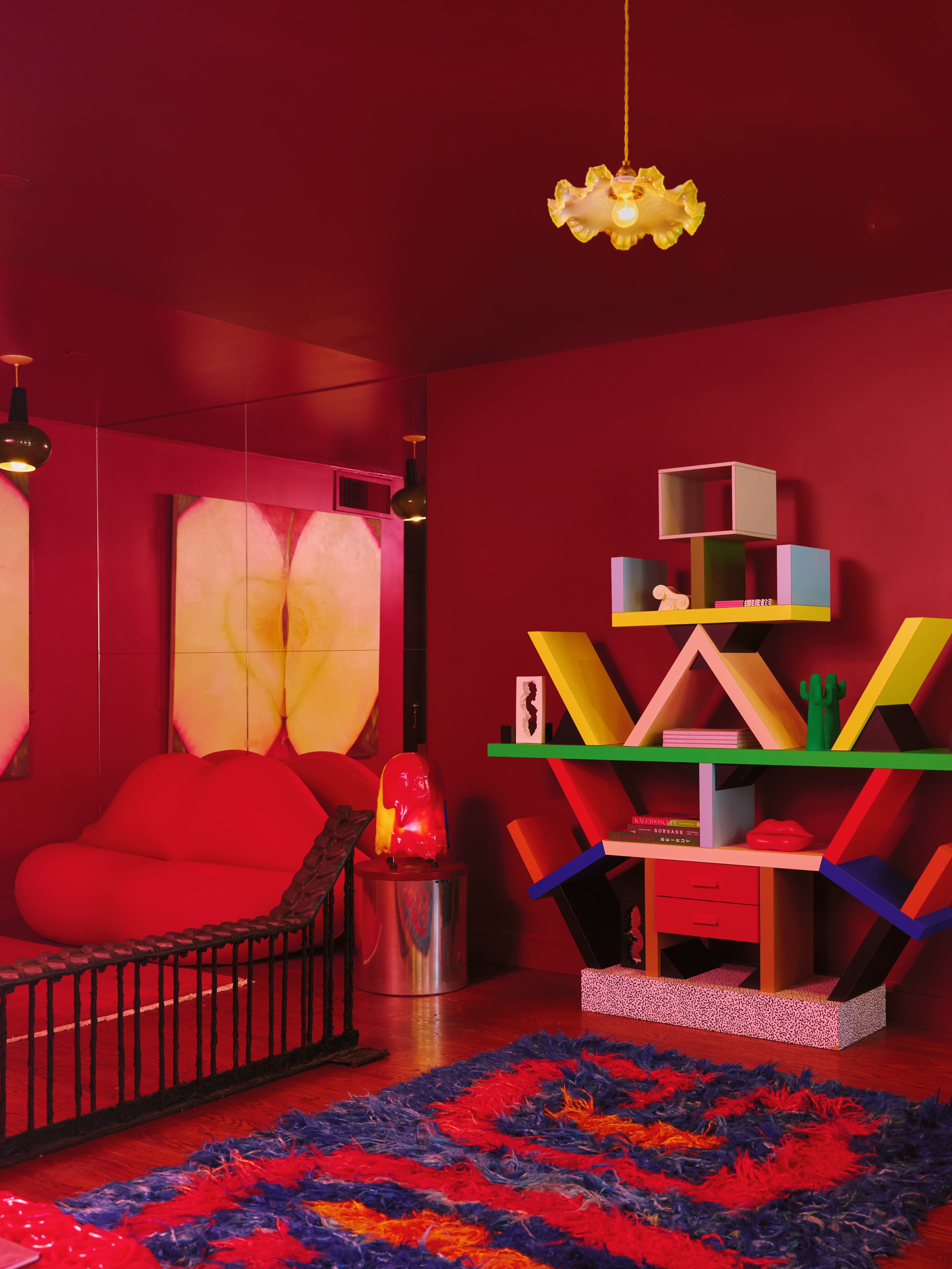The room features red walls and a vibrant multicolored shelf, alongside a plush red sofa and a colorful rug.
