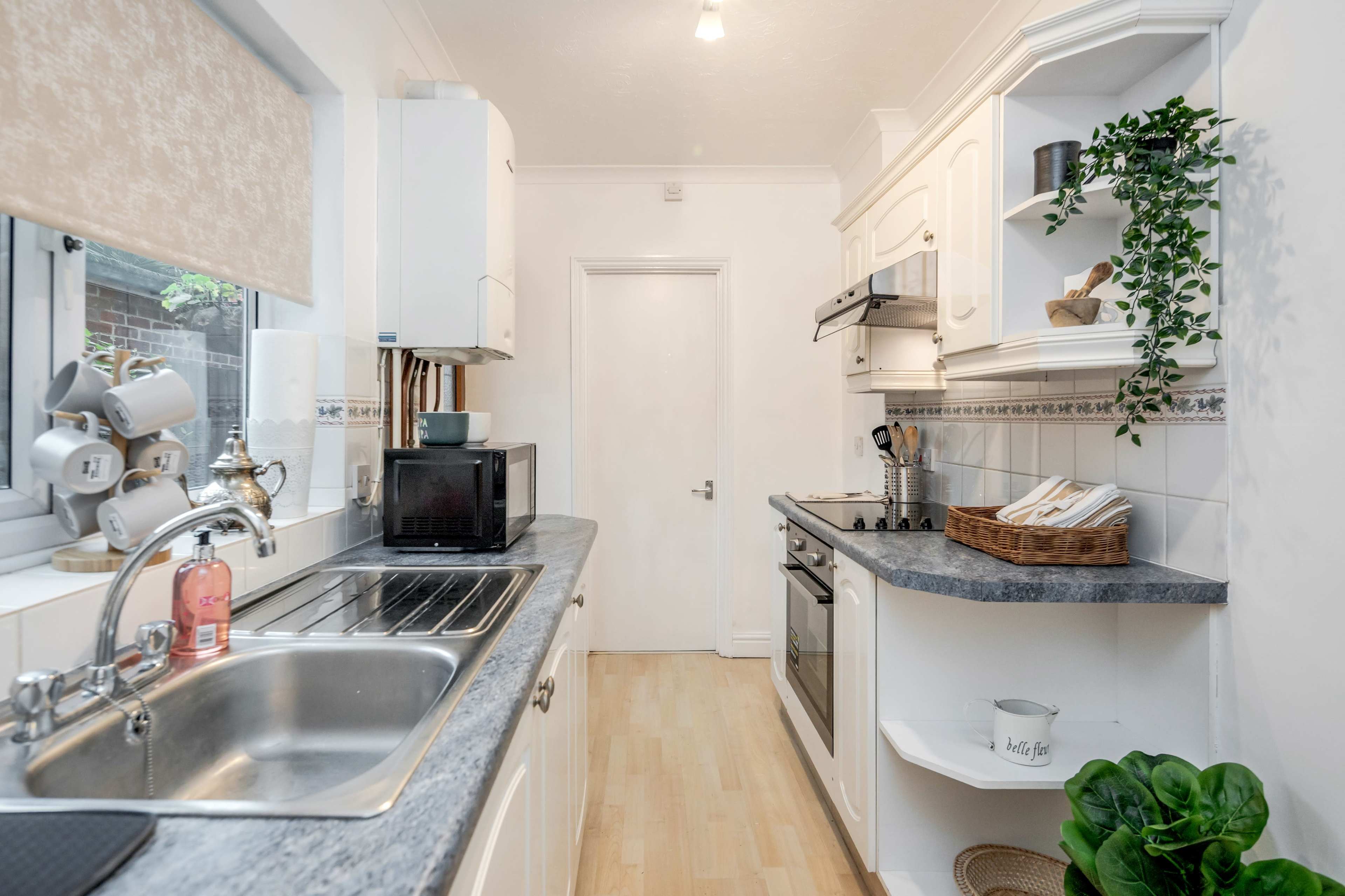 A compact kitchen features white cabinets, a sink, a countertop with a microwave, and a stove along one wall.
