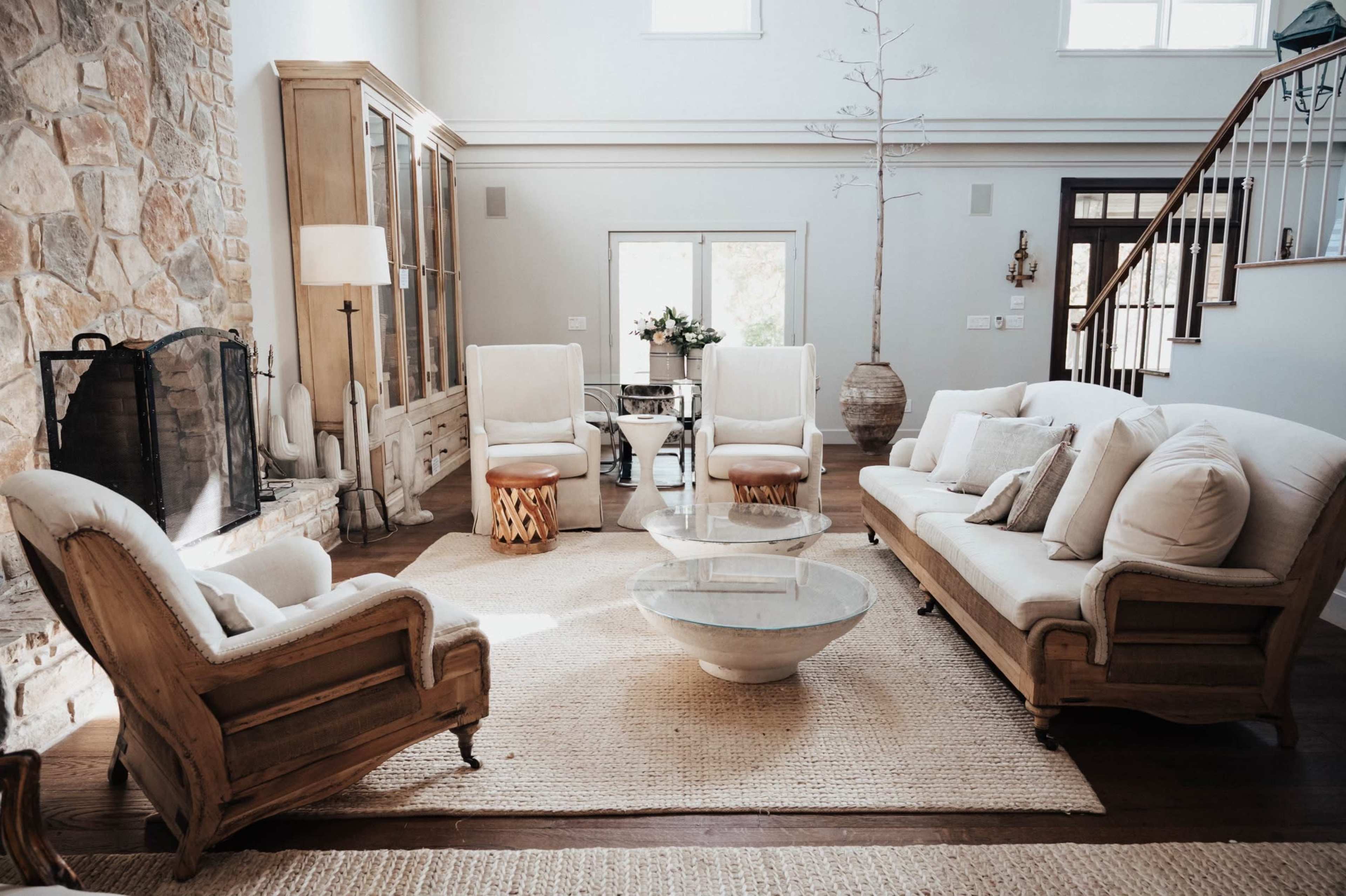The living room features a stone fireplace, a circular glass coffee table, and beige upholstered furniture arranged on a textured rug.