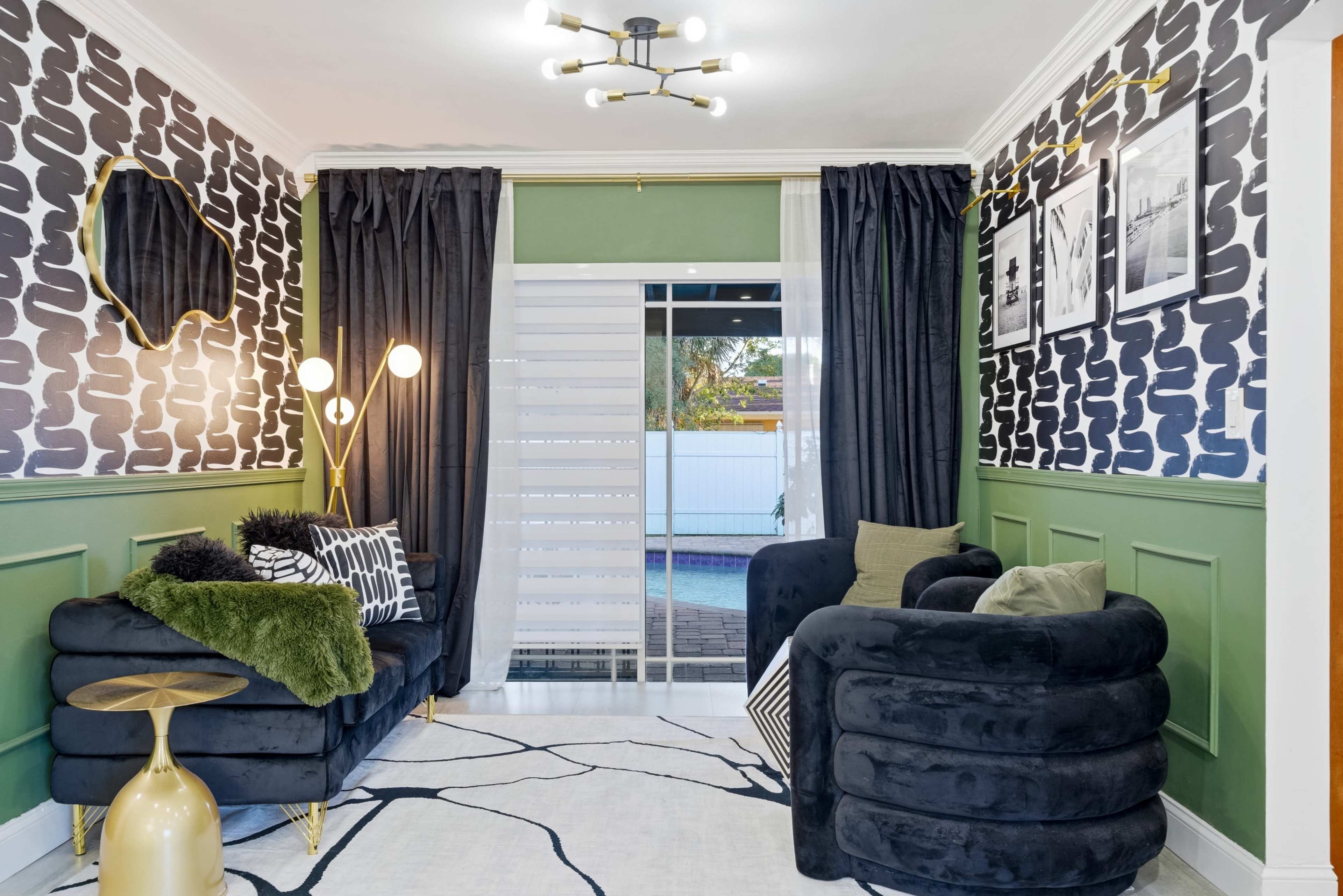 The image shows a stylish living room with dark patterned wallpaper, a green accent wall, black curtains, and modern furniture, including a plush sofa and a decorative table.