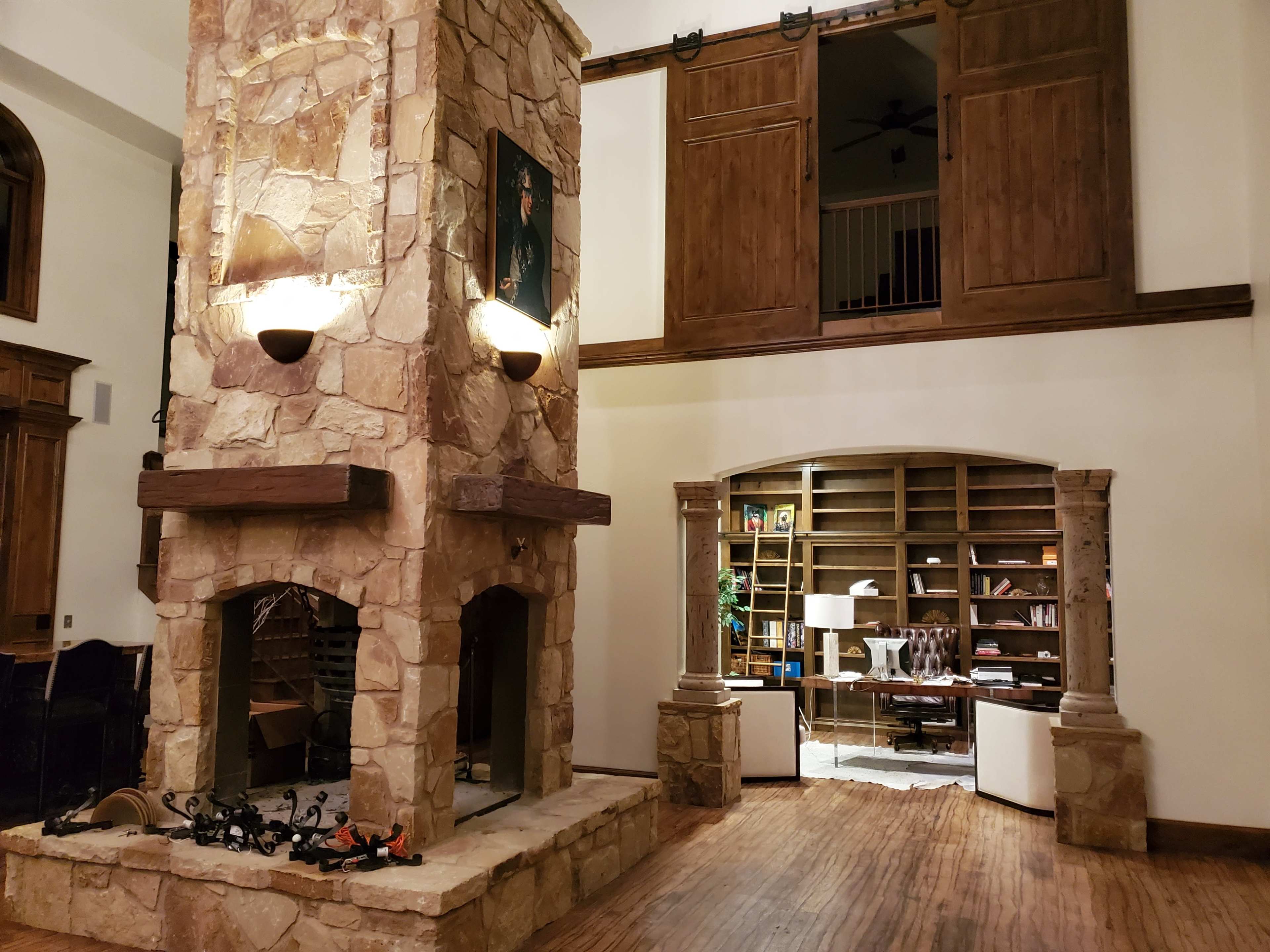 A large living room with a stone fireplace, wooden beams, and a loft area upstairs, featuring built-in shelves and a seating arrangement.