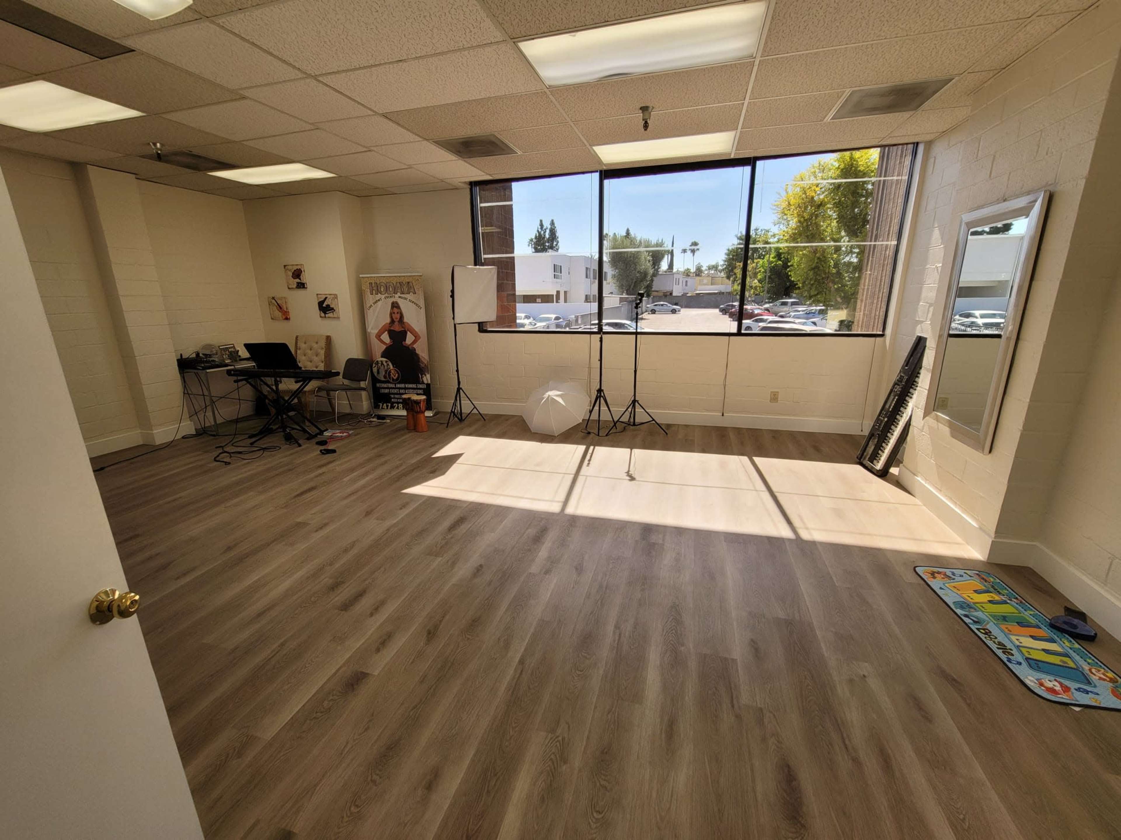 An empty, well-lit room with large windows, featuring a keyboard, photography equipment, and a mirror.