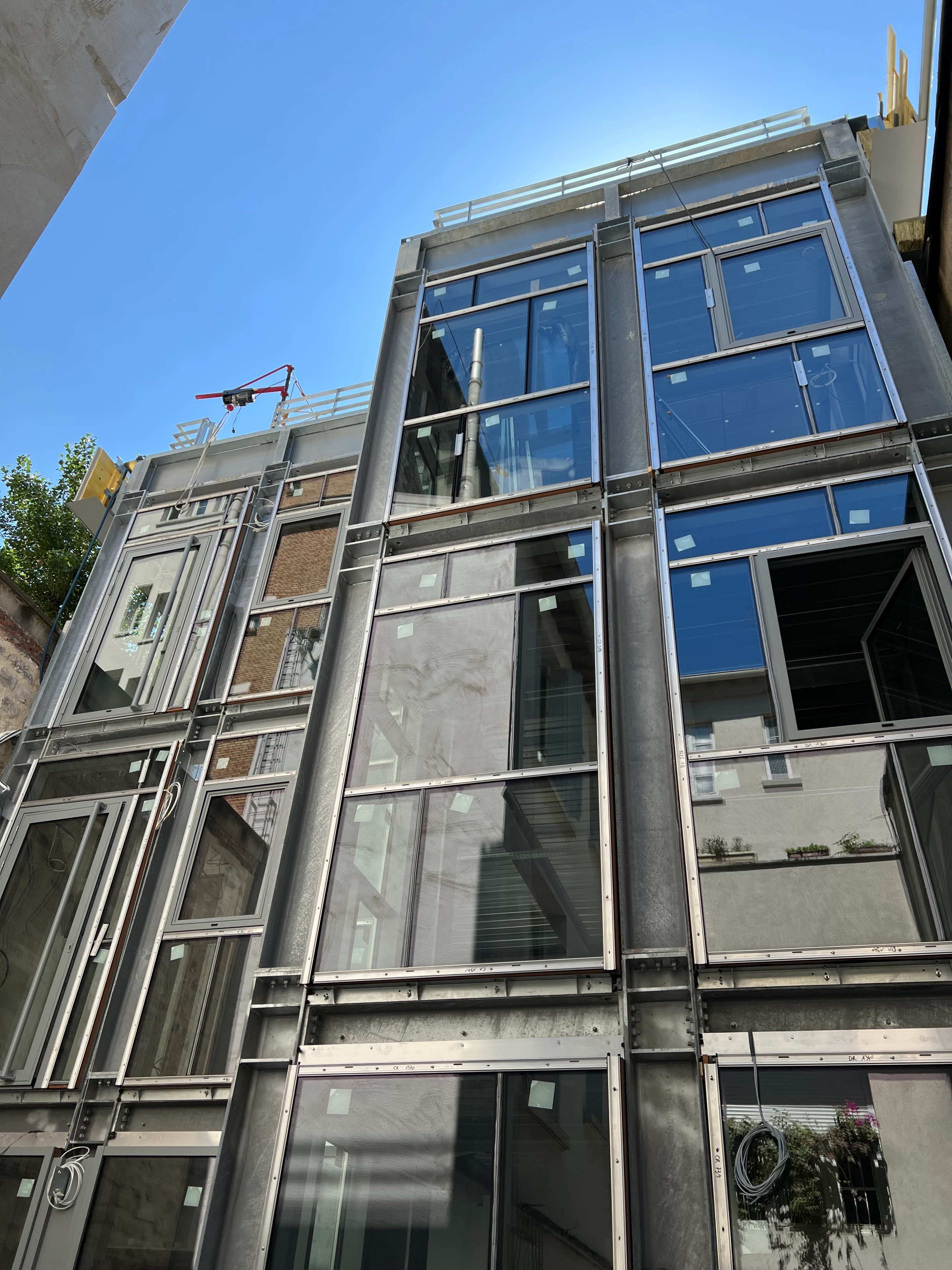 A modern building facade with multiple large windows and a metal frame structure under a clear blue sky.