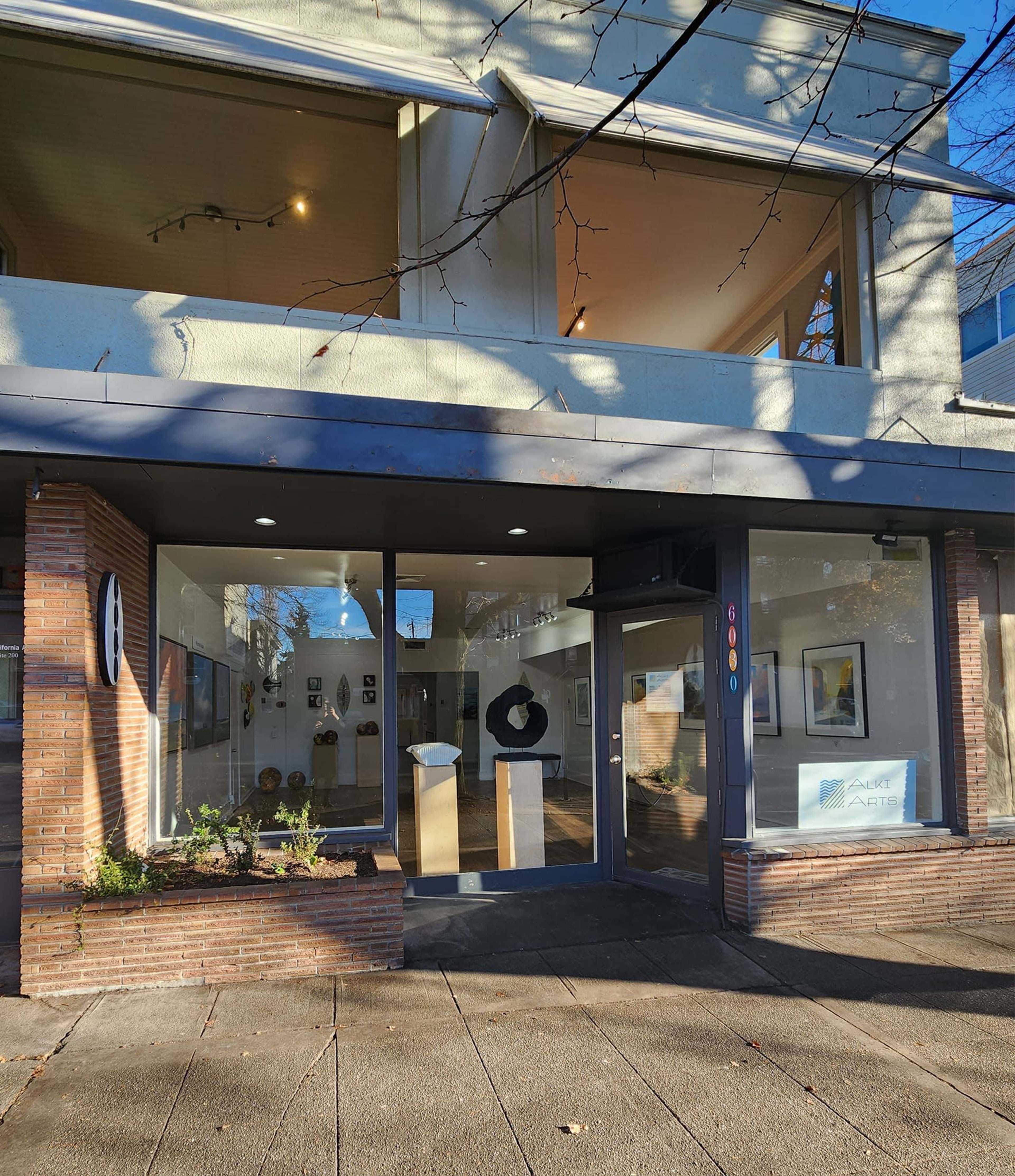 The exterior of an art gallery featuring a large glass window display, showcasing various artworks inside.