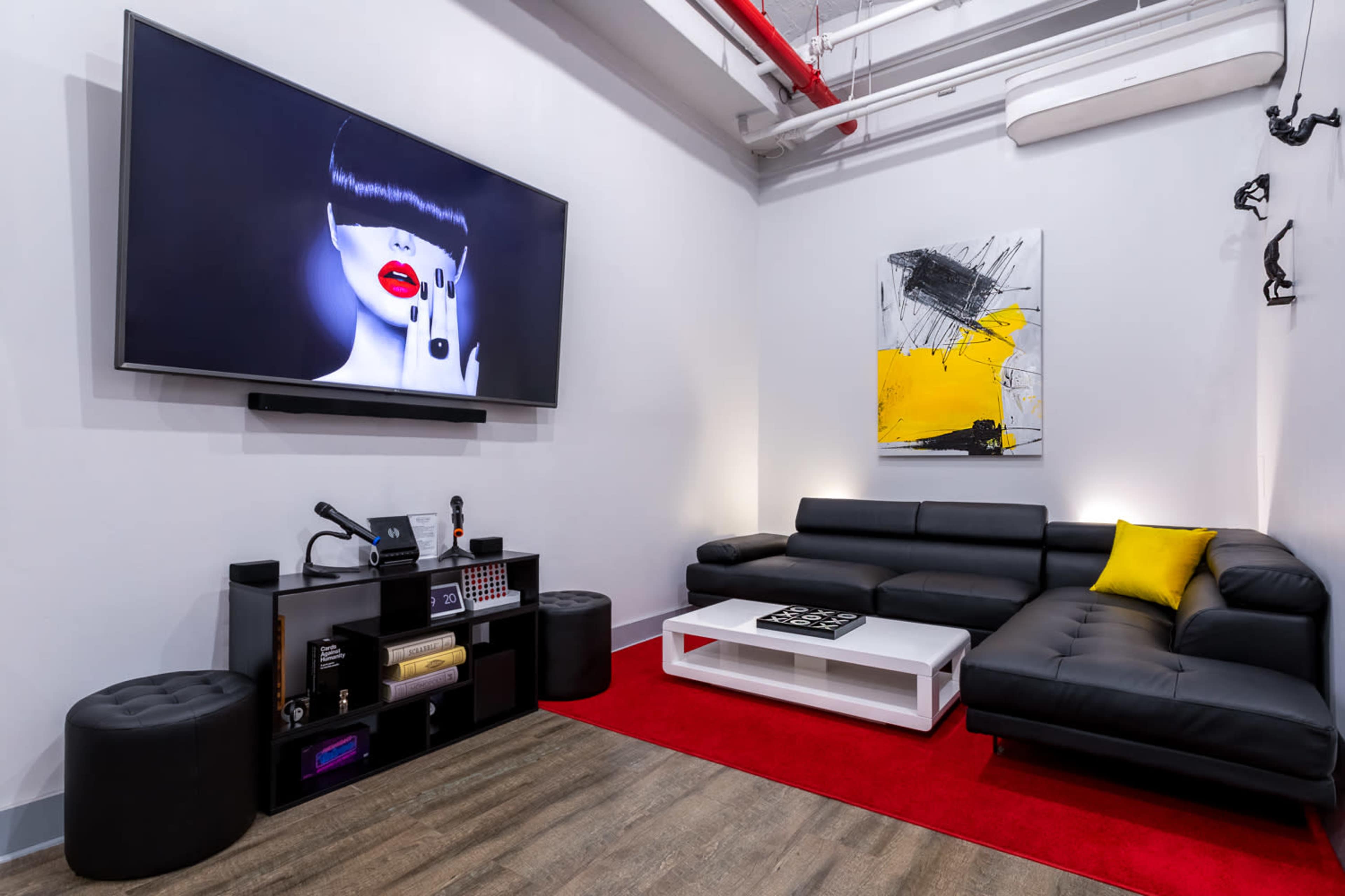 A modern living room featuring a large wall-mounted television, a black sectional sofa, a white coffee table, and abstract artwork on the wall.