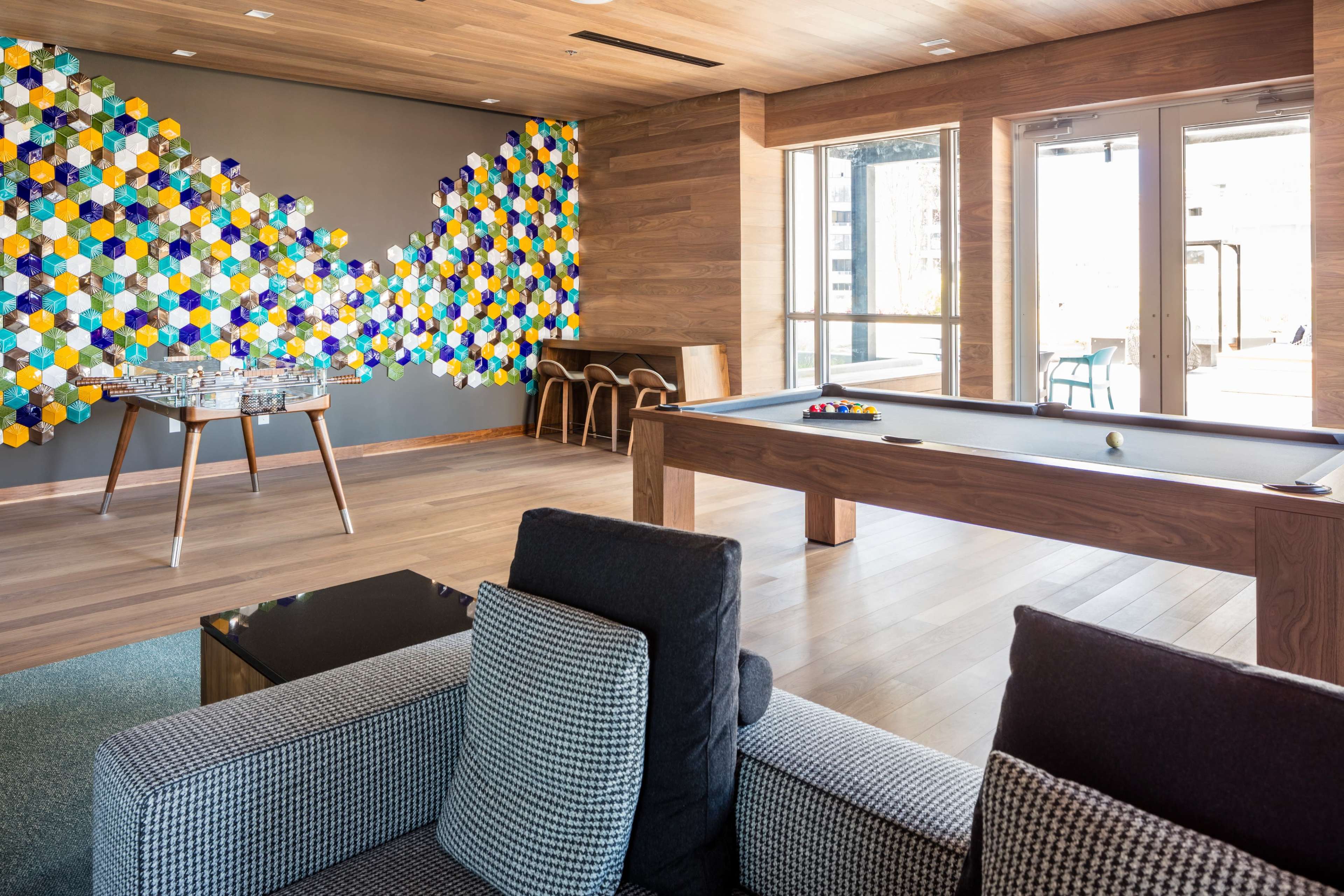 A modern indoor space featuring a colorful hexagonal-patterned wall, a billiard table, and comfortable seating.