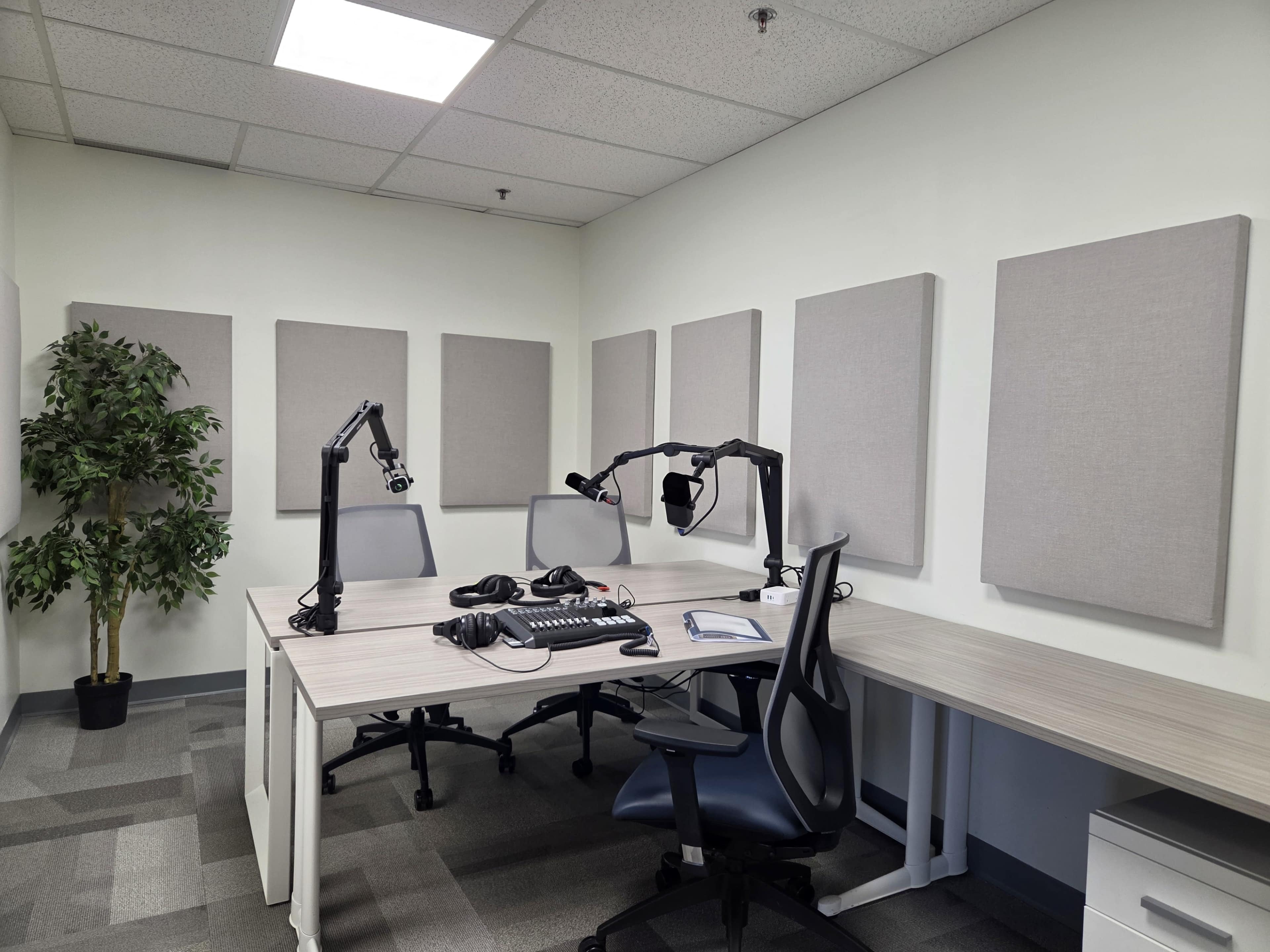 The image shows a small recording studio with soundproof wall panels, two desks with chairs, and audio equipment in the center.