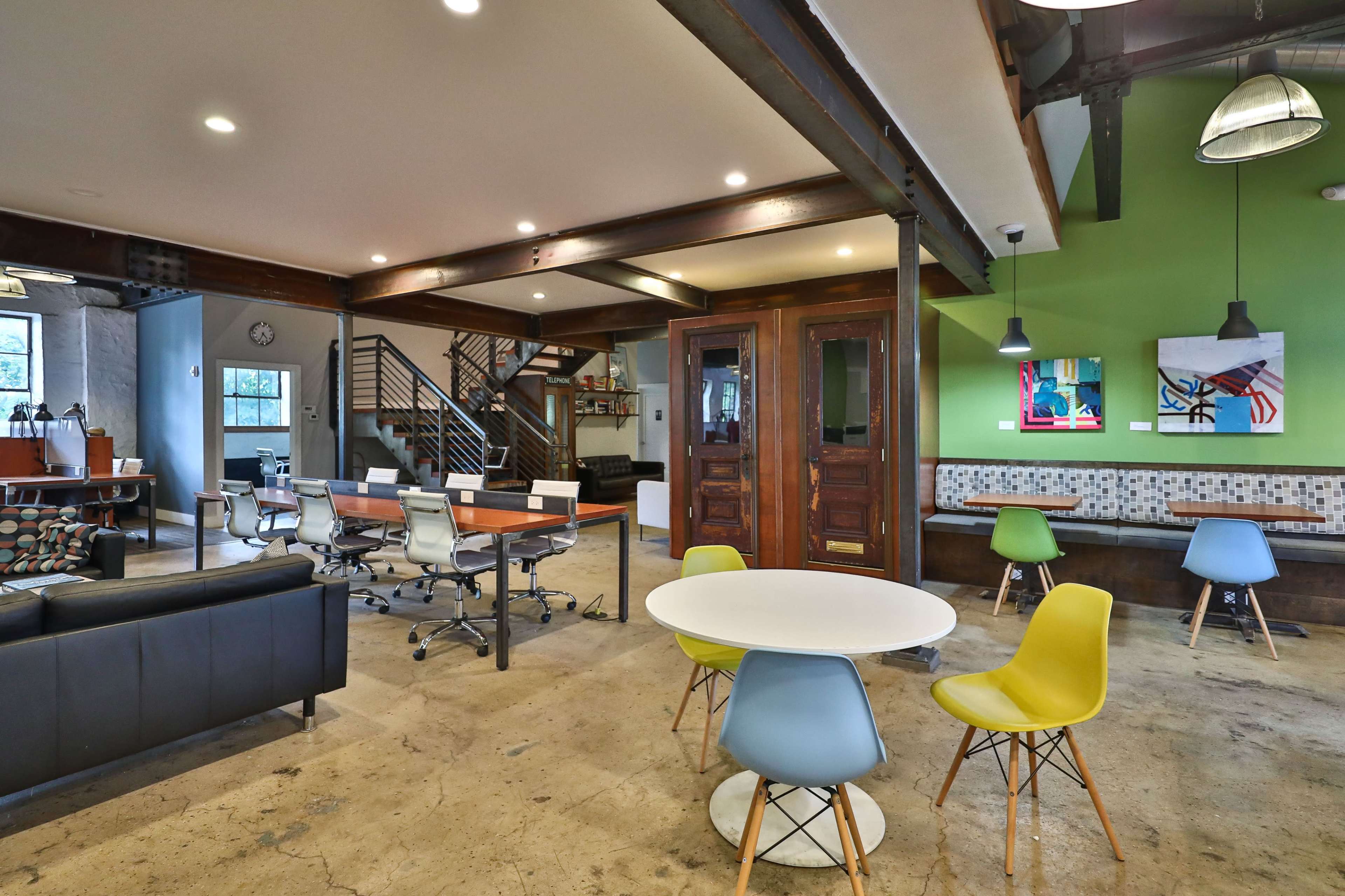 A modern open office space featuring a mix of workstations, seating areas, and colorful chairs against a backdrop of exposed beams and industrial design elements.