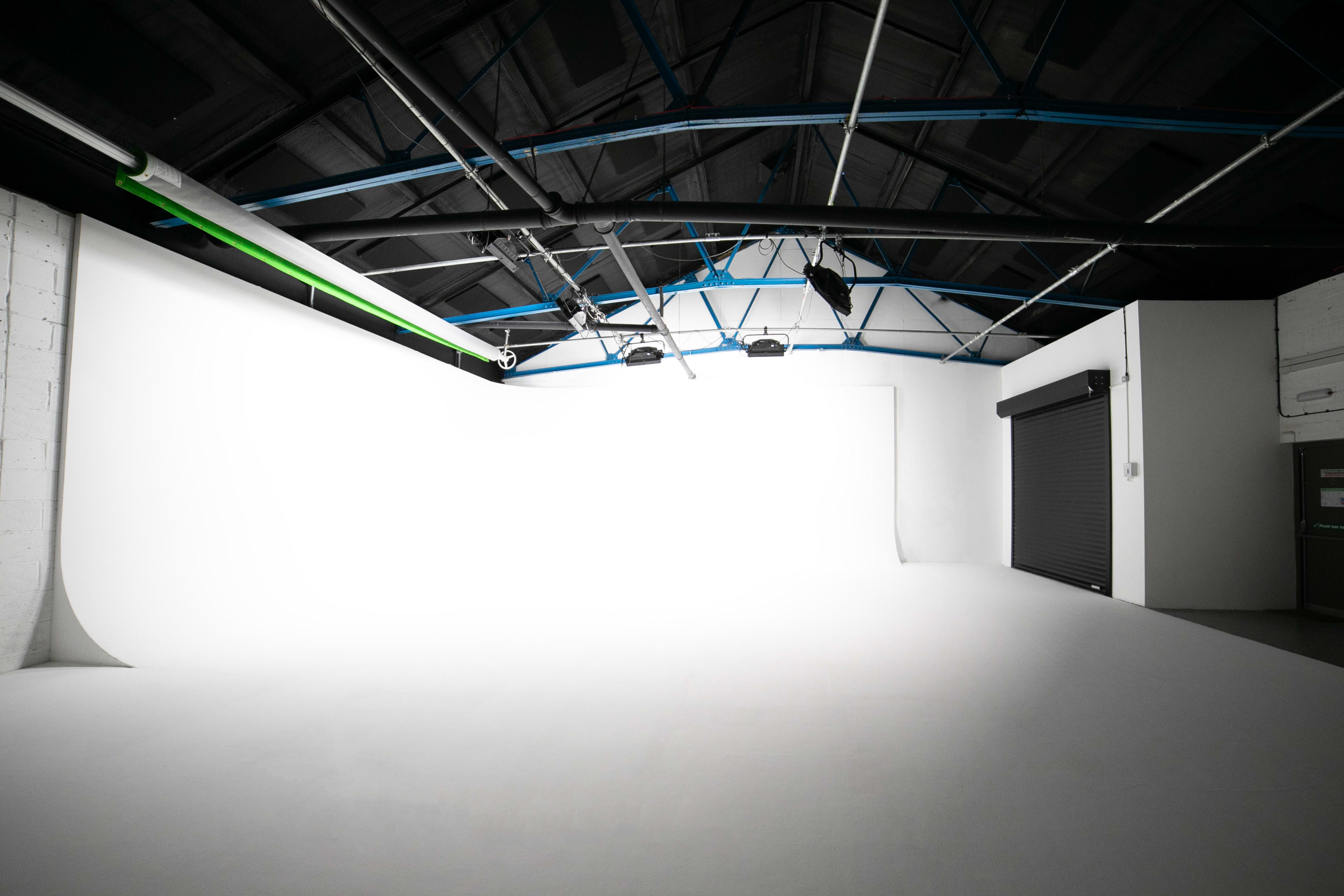 The image shows a spacious photography studio with a white seamless backdrop and a partially closed garage door.