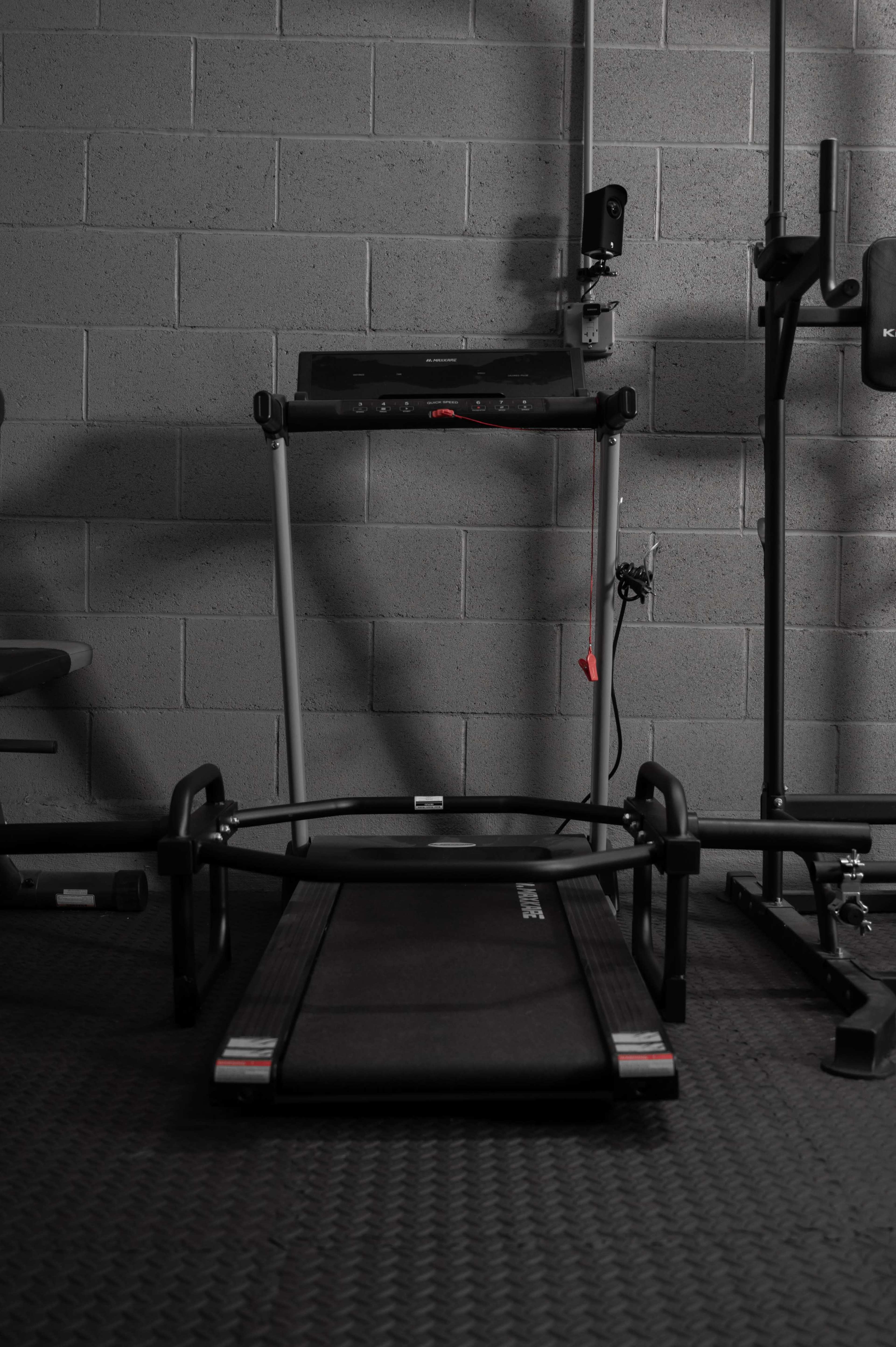 A treadmill in a minimalistic gym setting with various exercise equipment surrounding it.
