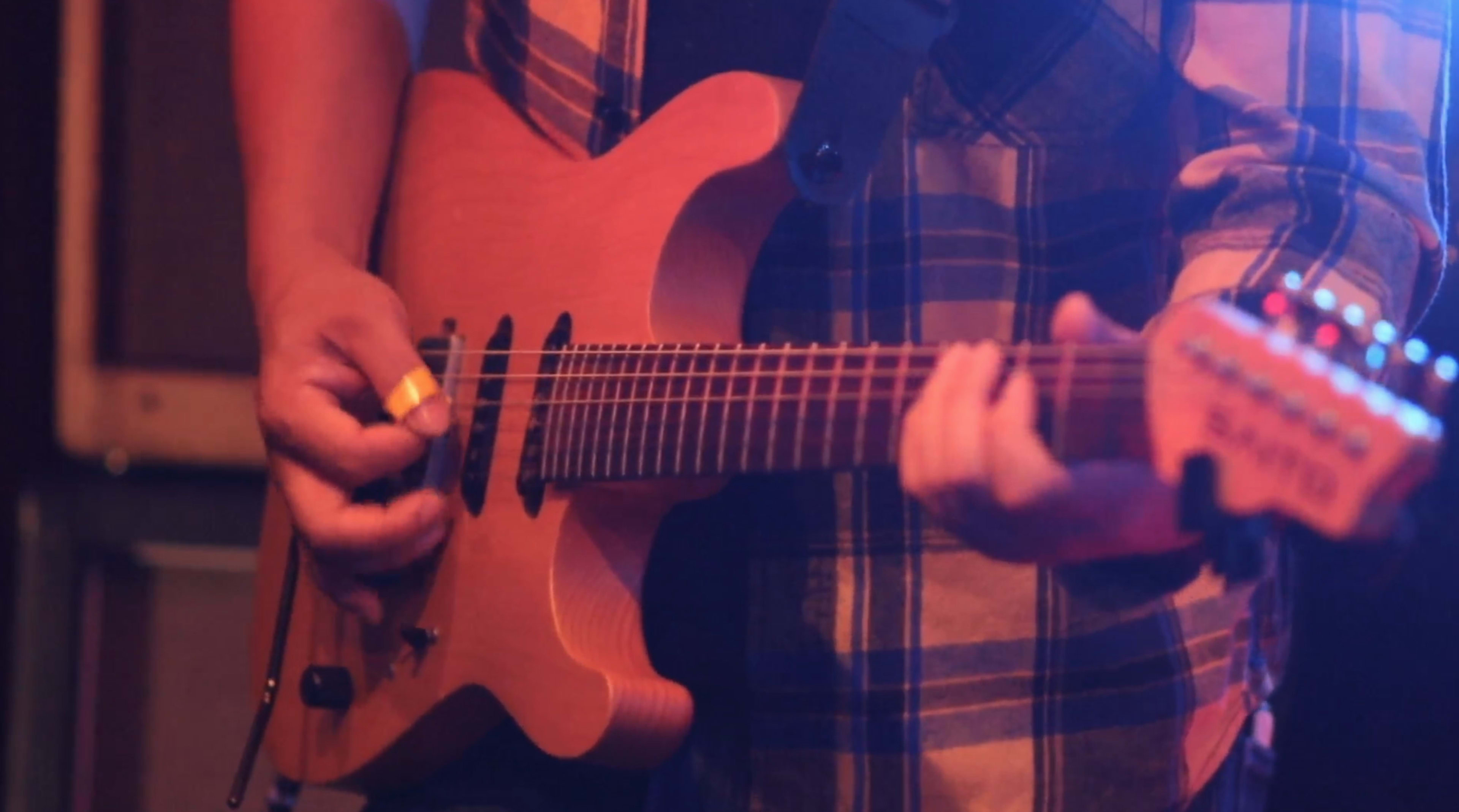 A person plays a wooden electric guitar while wearing a plaid shirt.