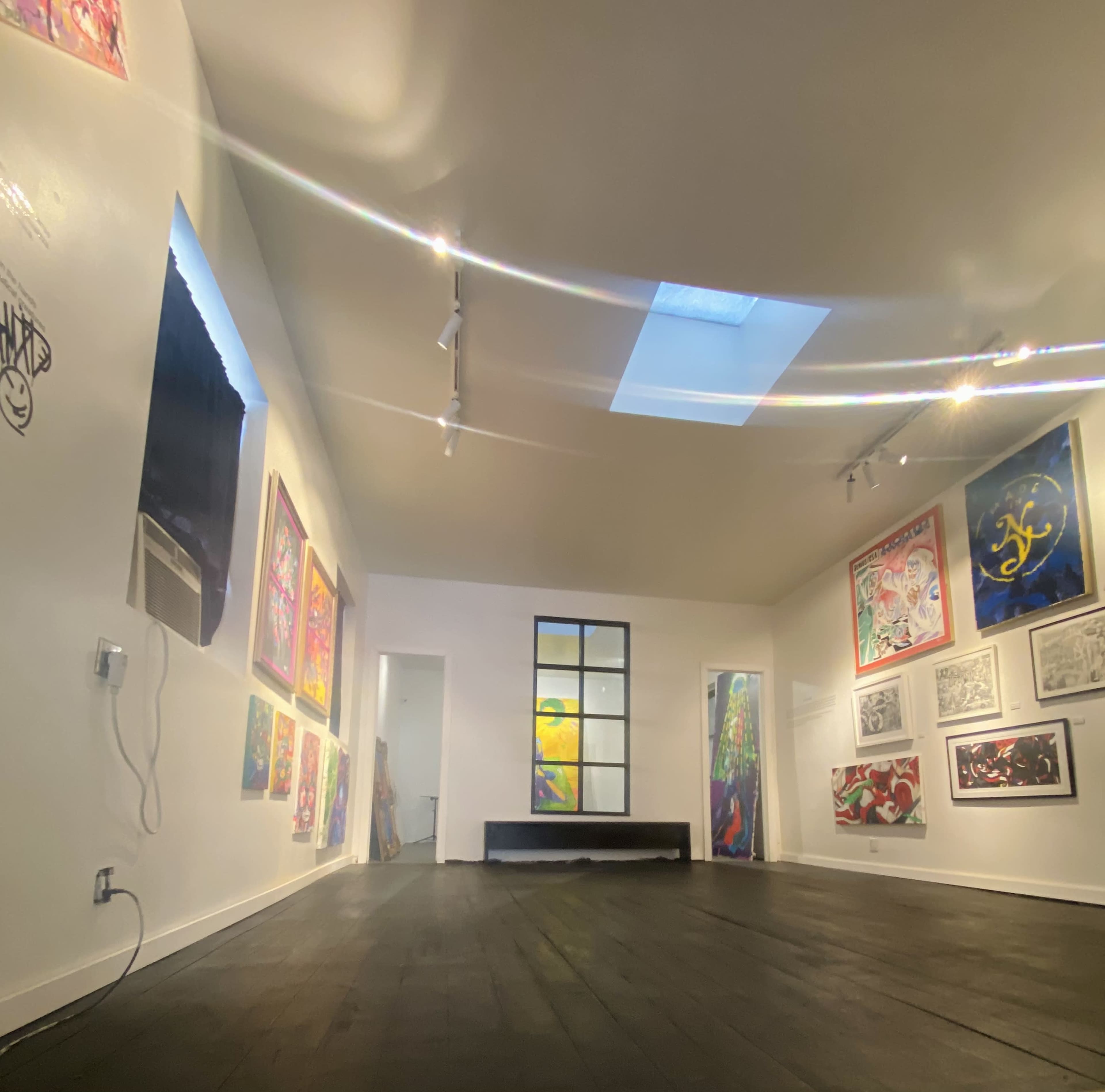 The image shows an art gallery with colorful paintings on the white walls and a large skylight above.
