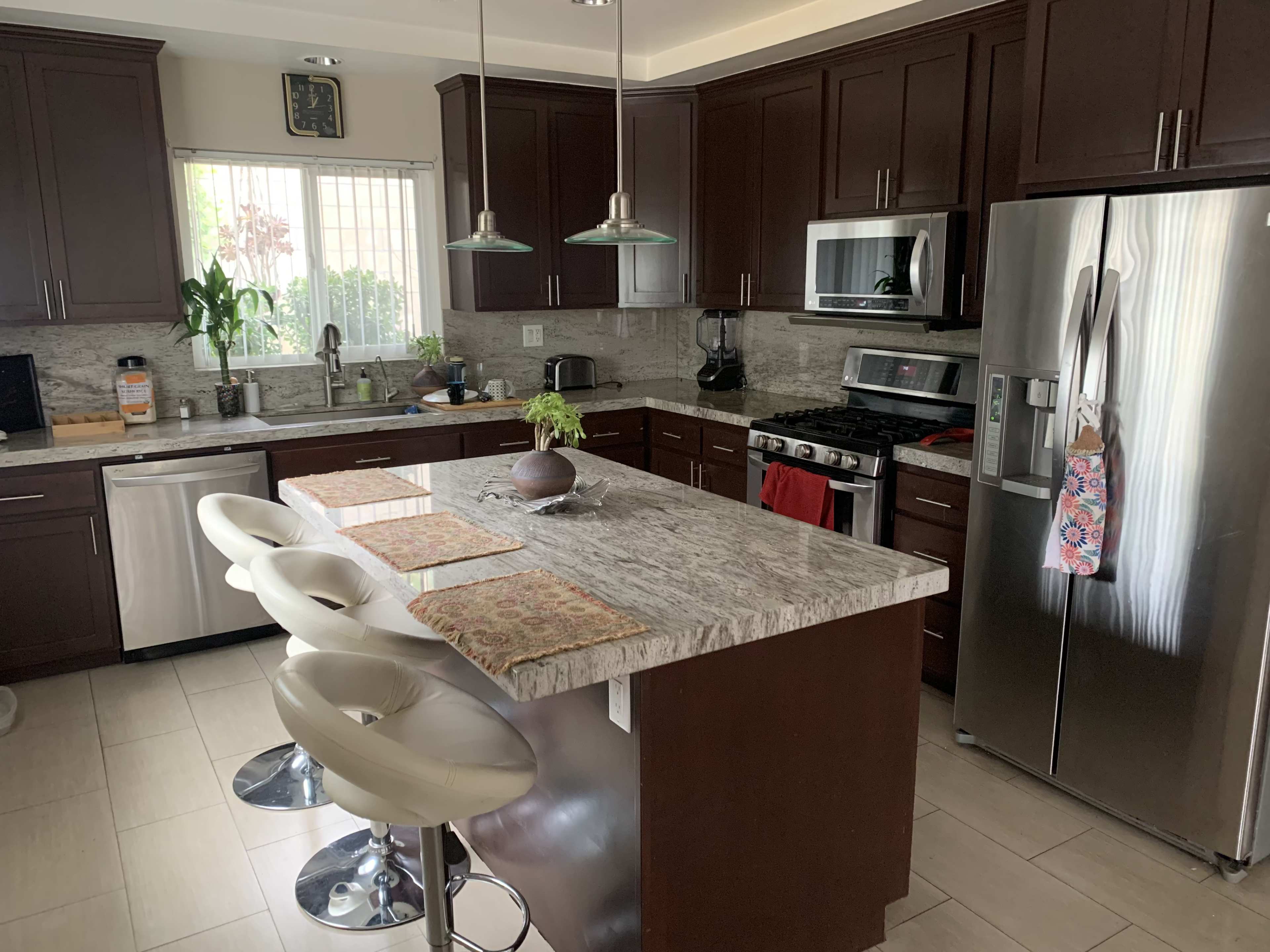 A modern kitchen with dark wooden cabinets, a granite countertop island with four white bar stools, and stainless steel appliances.