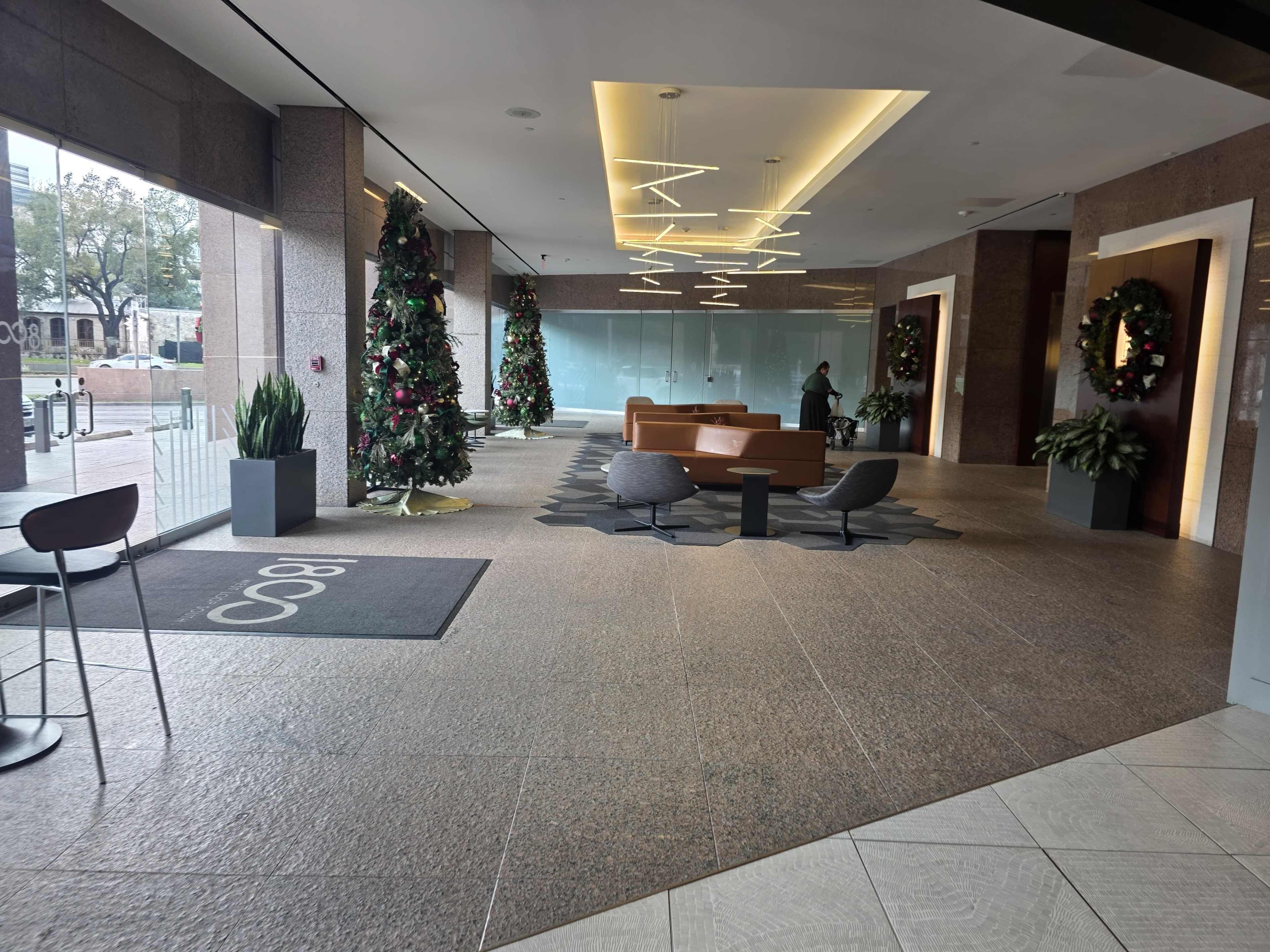 The lobby features two Christmas trees, modern furniture, and a minimalist design with decorative wreaths on the doors.