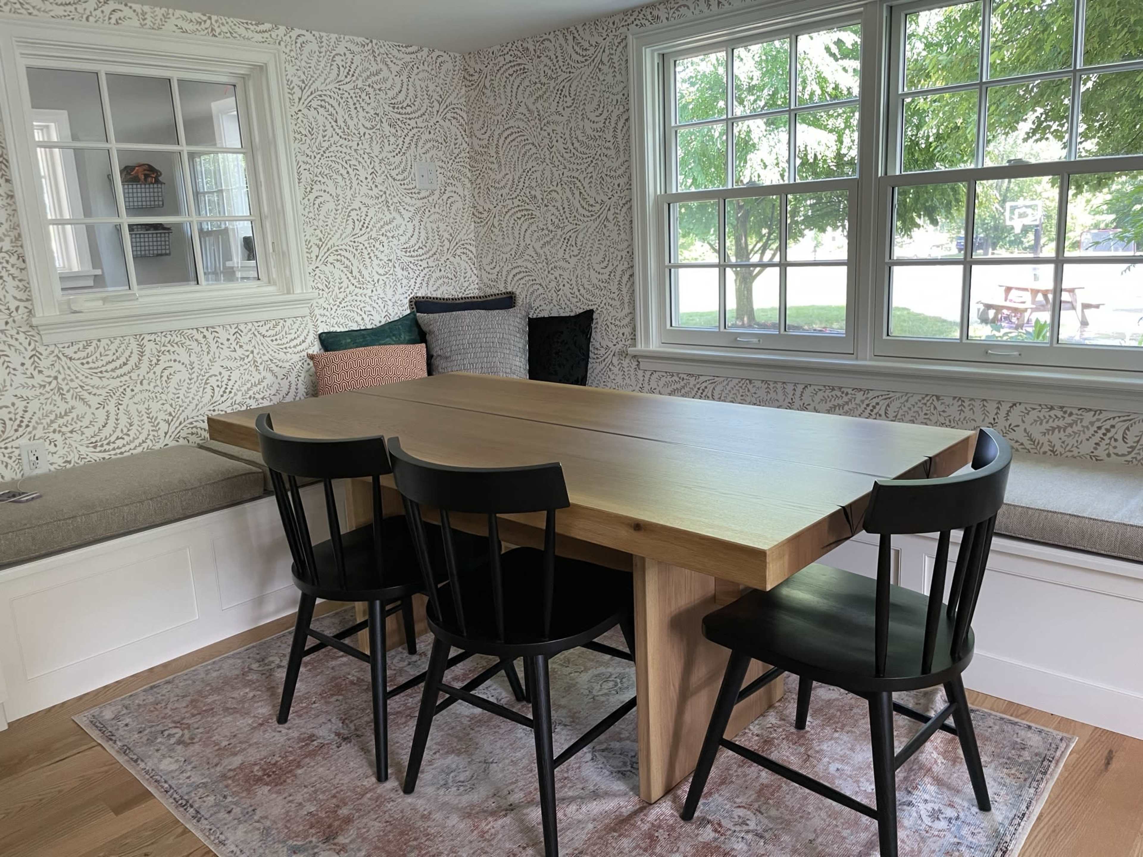 A dining area with a wooden table surrounded by four black chairs and a cozy window seat with cushions.