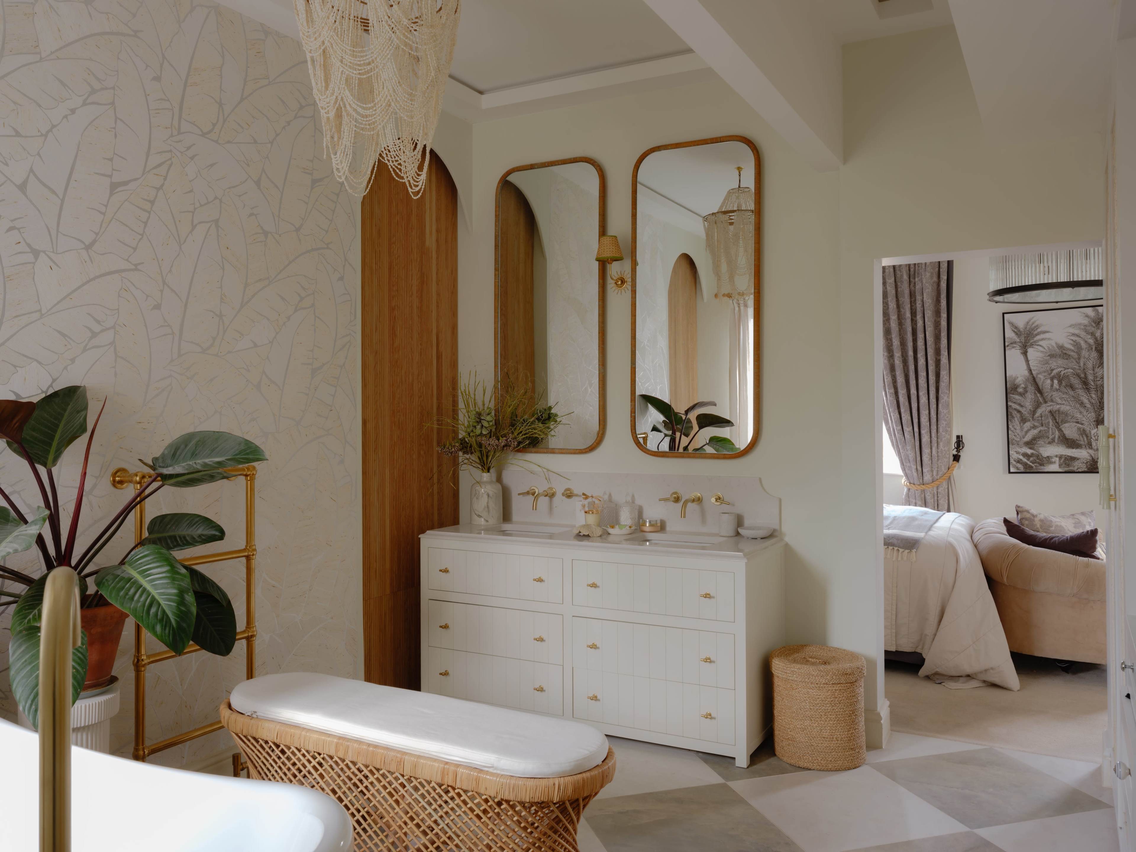 A modern bathroom features a sleek white vanity with three mirrors, a woven bench, and a decorative plant, complemented by light-colored walls and a doorway leading to a bedroom.