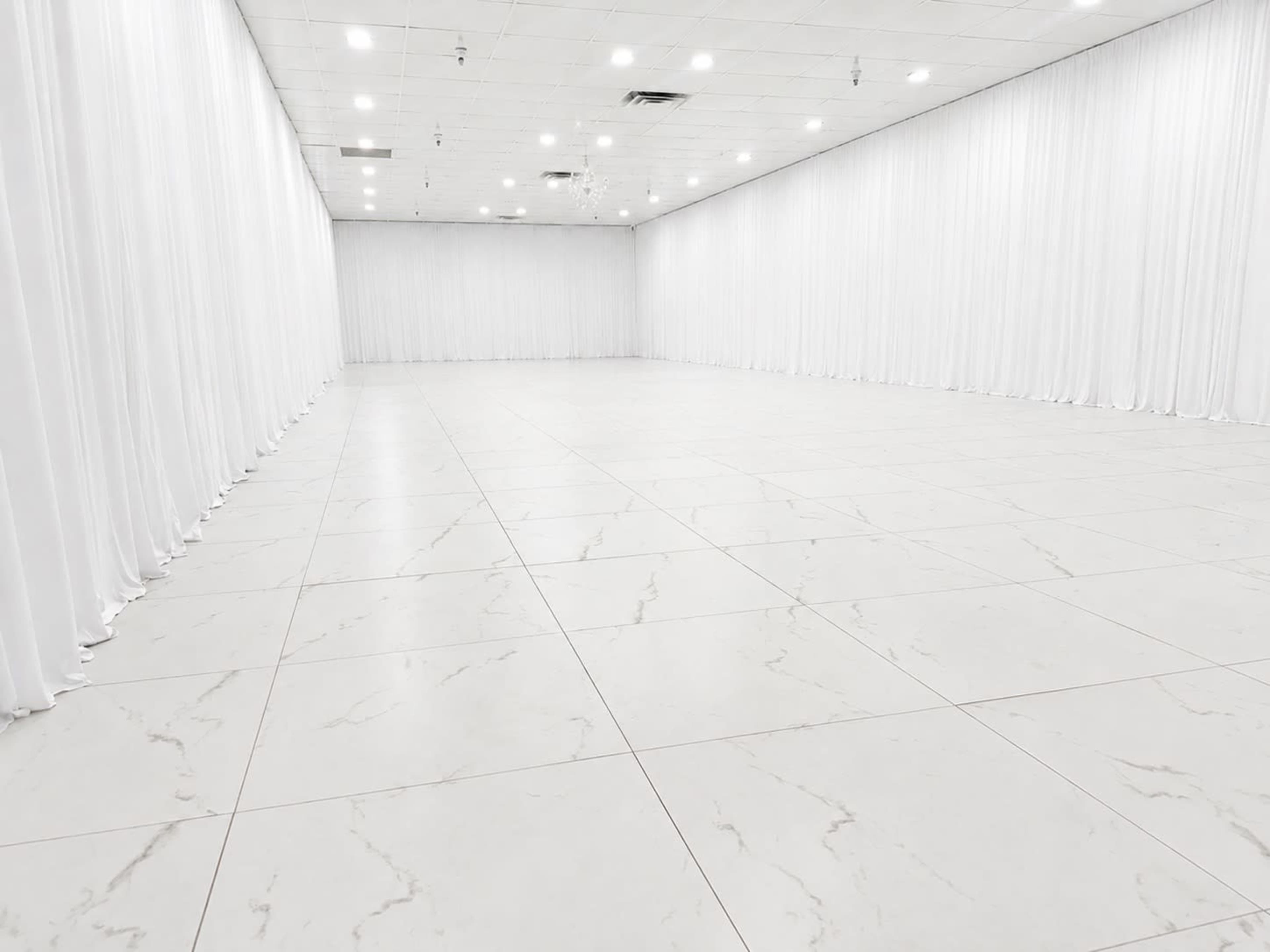 The image shows a spacious, empty room with white walls and floor, adorned with long white curtains along one side.
