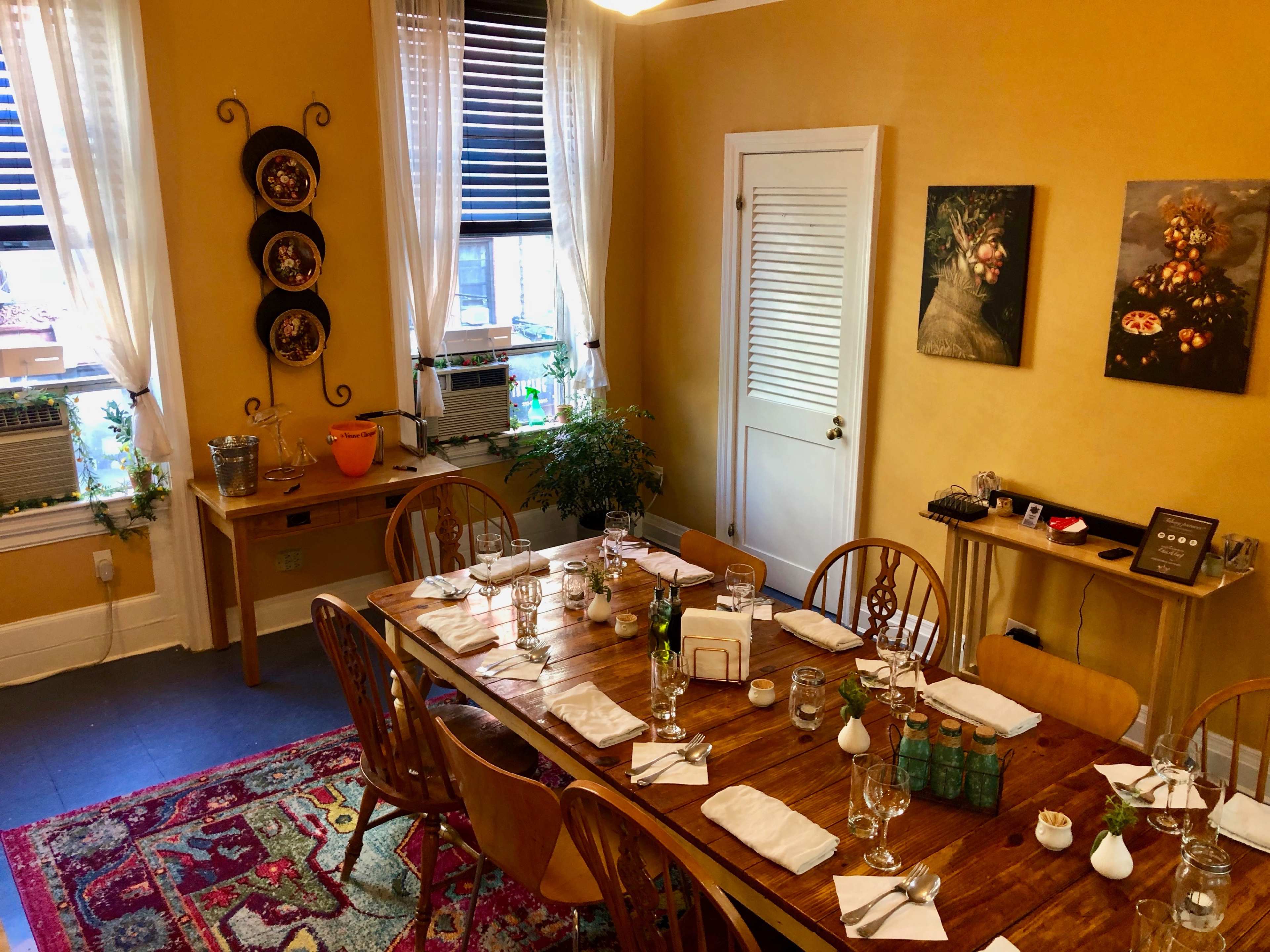 A well-set dining table is arranged with utensils and glassware in a warm, yellow-walled room featuring two pieces of framed art.