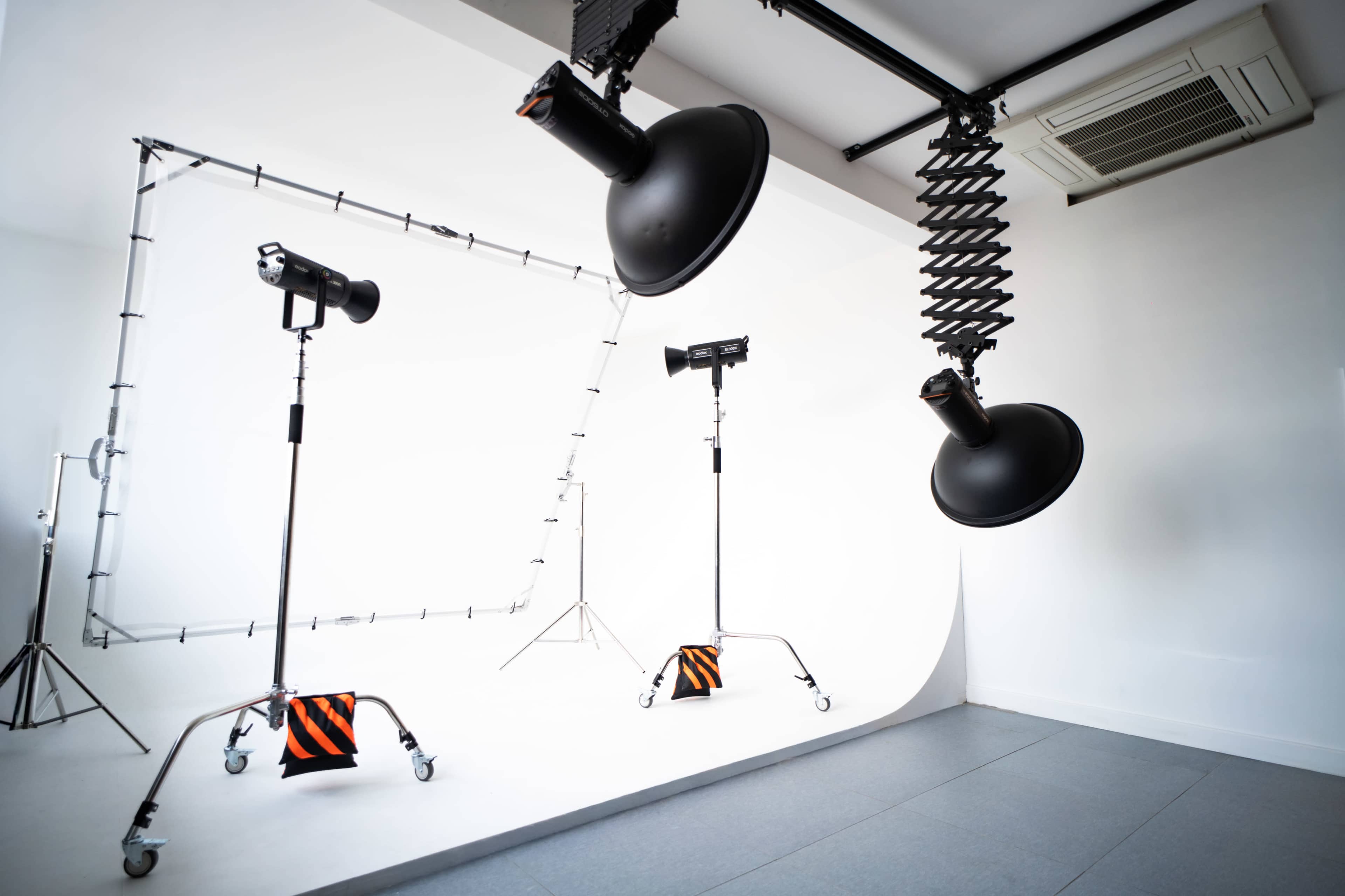 The image shows a photography studio with three lighting fixtures and a white backdrop.