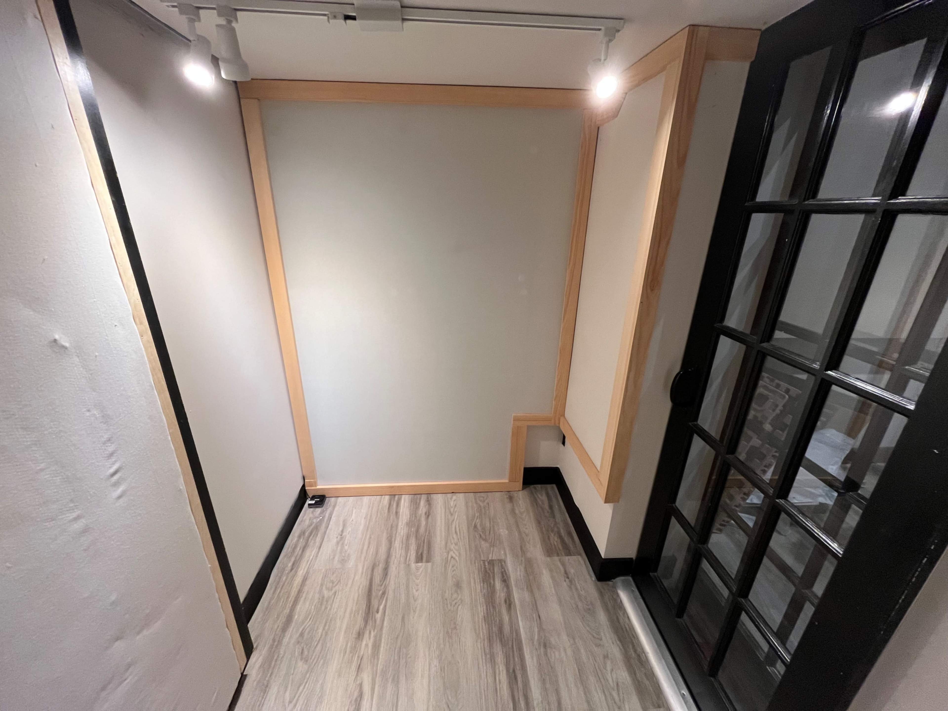 The image shows a small, partially enclosed room with wooden accents, a light fixture, and a clean floor.