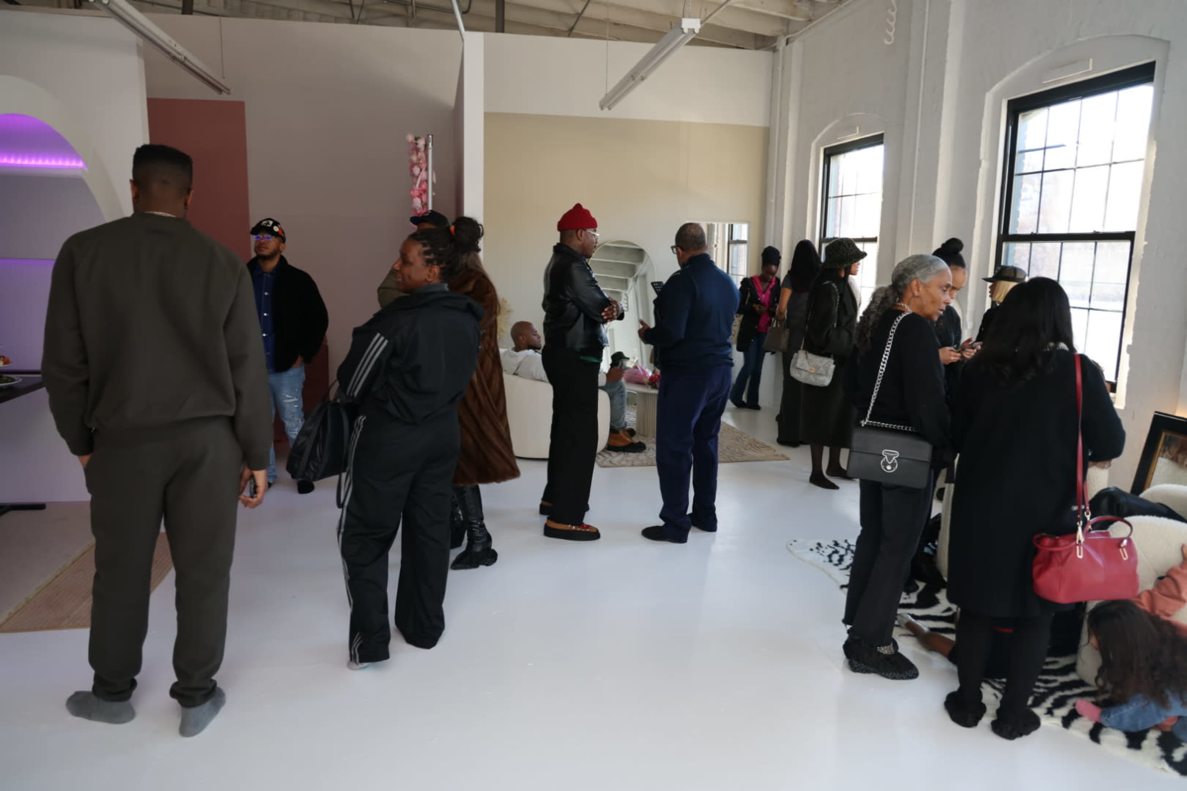 A group of people stands and socializes in a modern, well-lit gallery space with large windows.
