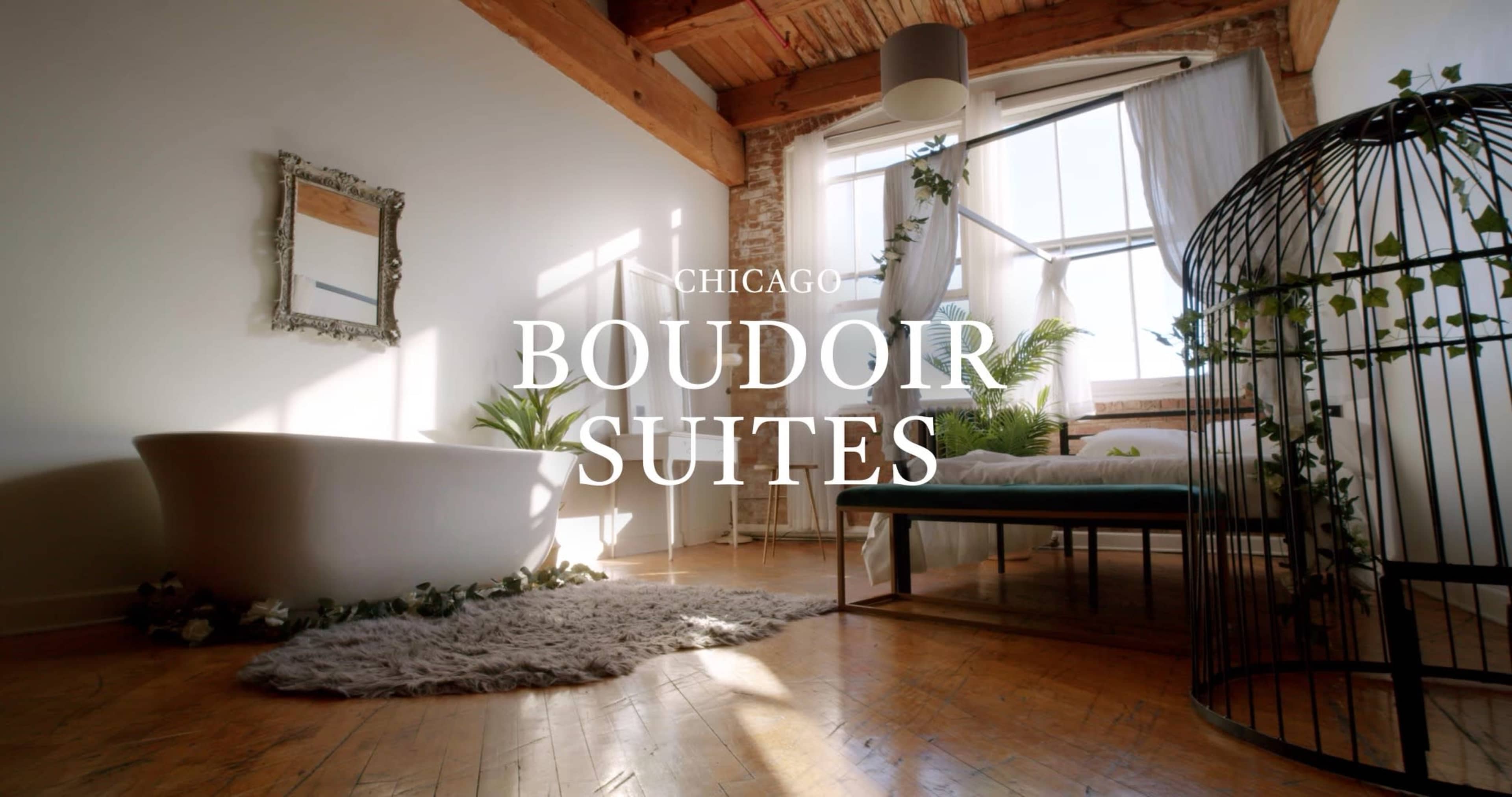 A bright, airy room with a freestanding bathtub, a bed, and greenery, featuring large windows and wooden beams.