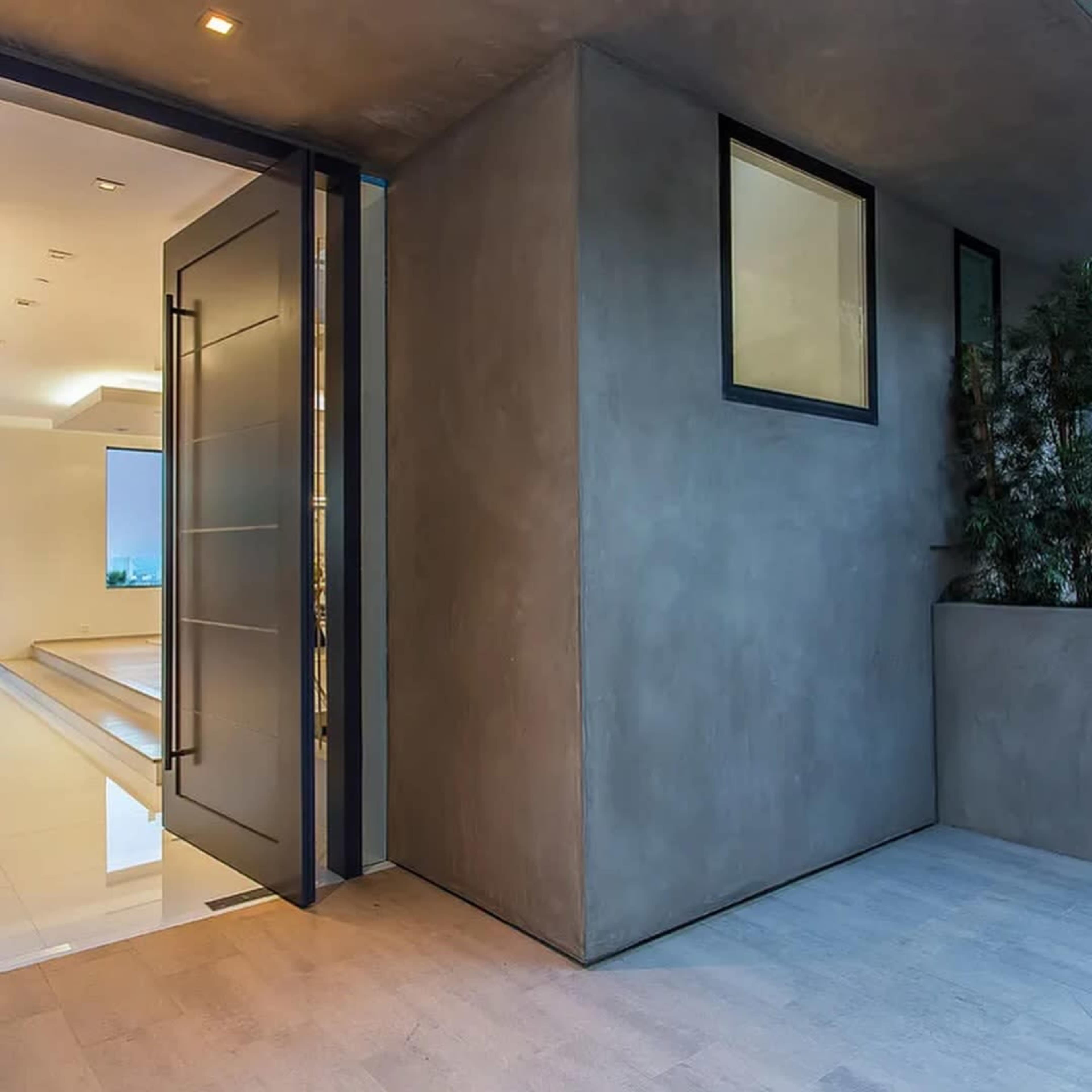 A large modern door stands partially open, revealing a well-lit interior with minimalist design elements and a polished floor.