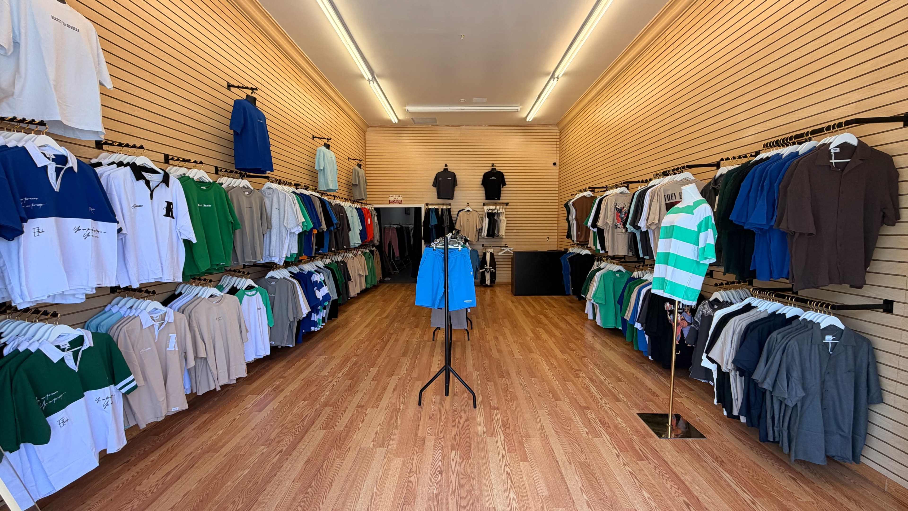 A clothing store displays a variety of shirts arranged neatly on racks along the walls and on a central stand.