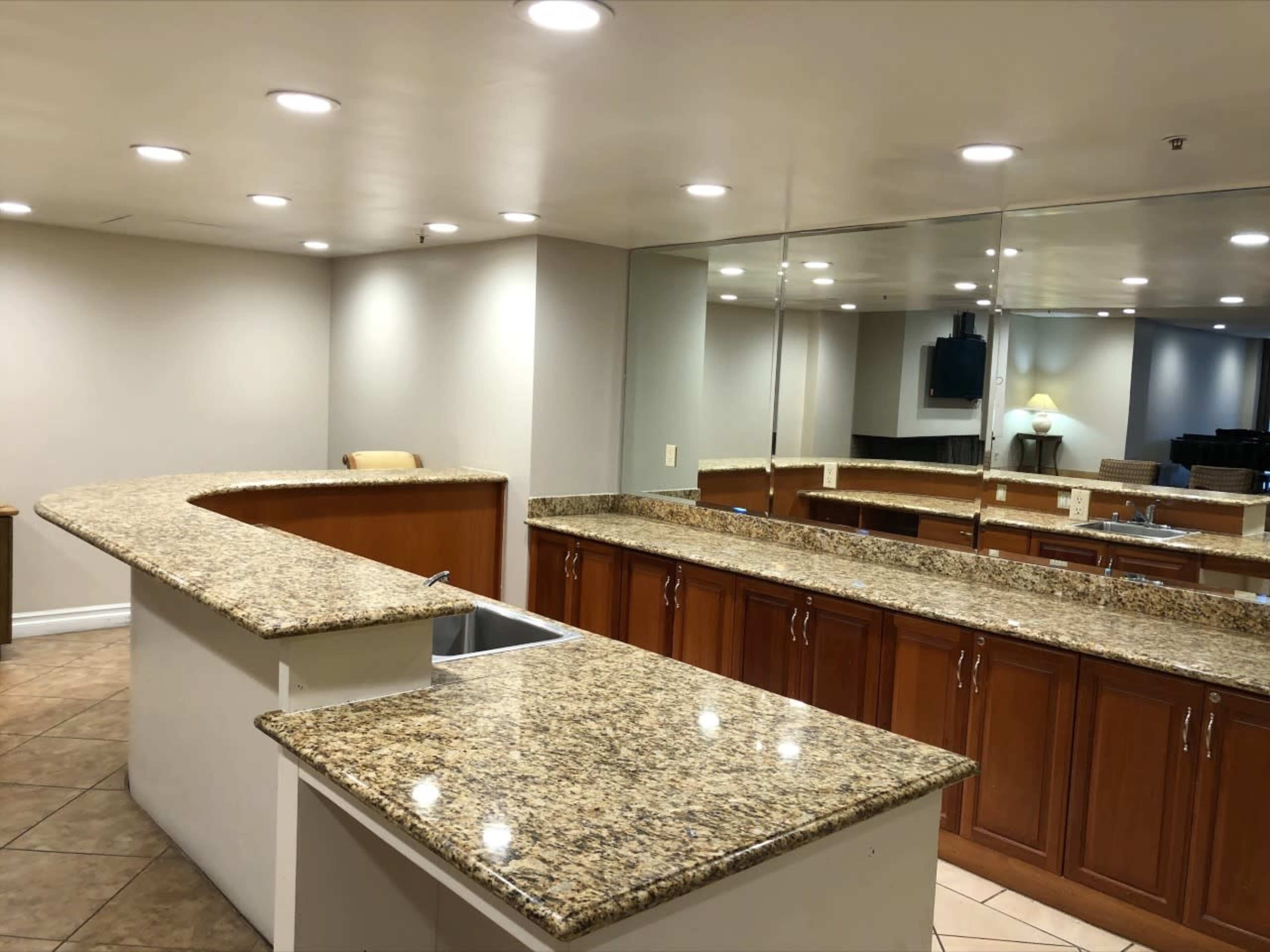 A kitchen area with a long granite countertop, wooden cabinets, and a mirrored wall.